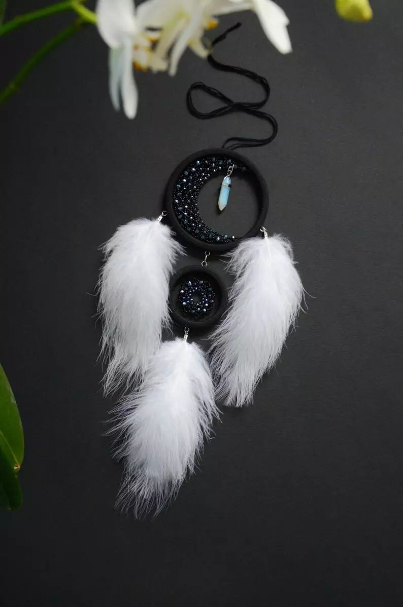 Handmade crescent moon dreamcatcher with white feathers, black aventurine crystals, and a moonstone pendant, designed for boho decor, spiritual protection, and a mystical ambiance.