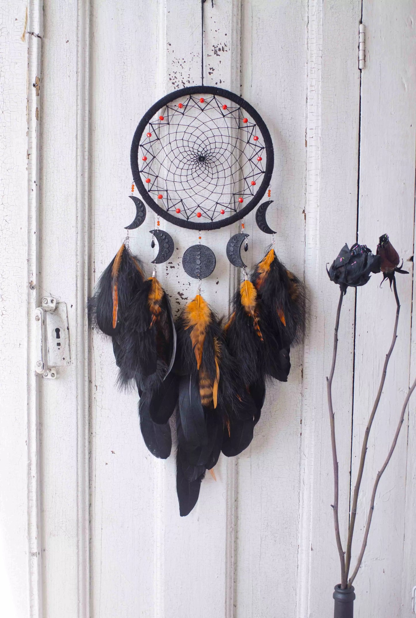Handcrafted black dream catcher featuring an intricate web design with crescent moon charms and vibrant orange feathers. This bohemian wall decor piece is perfect for capturing negative dreams and channeling positive energy. Ideal for enhancing the aesthetic of any home or office space and makes a thoughtful, spiritual gift.