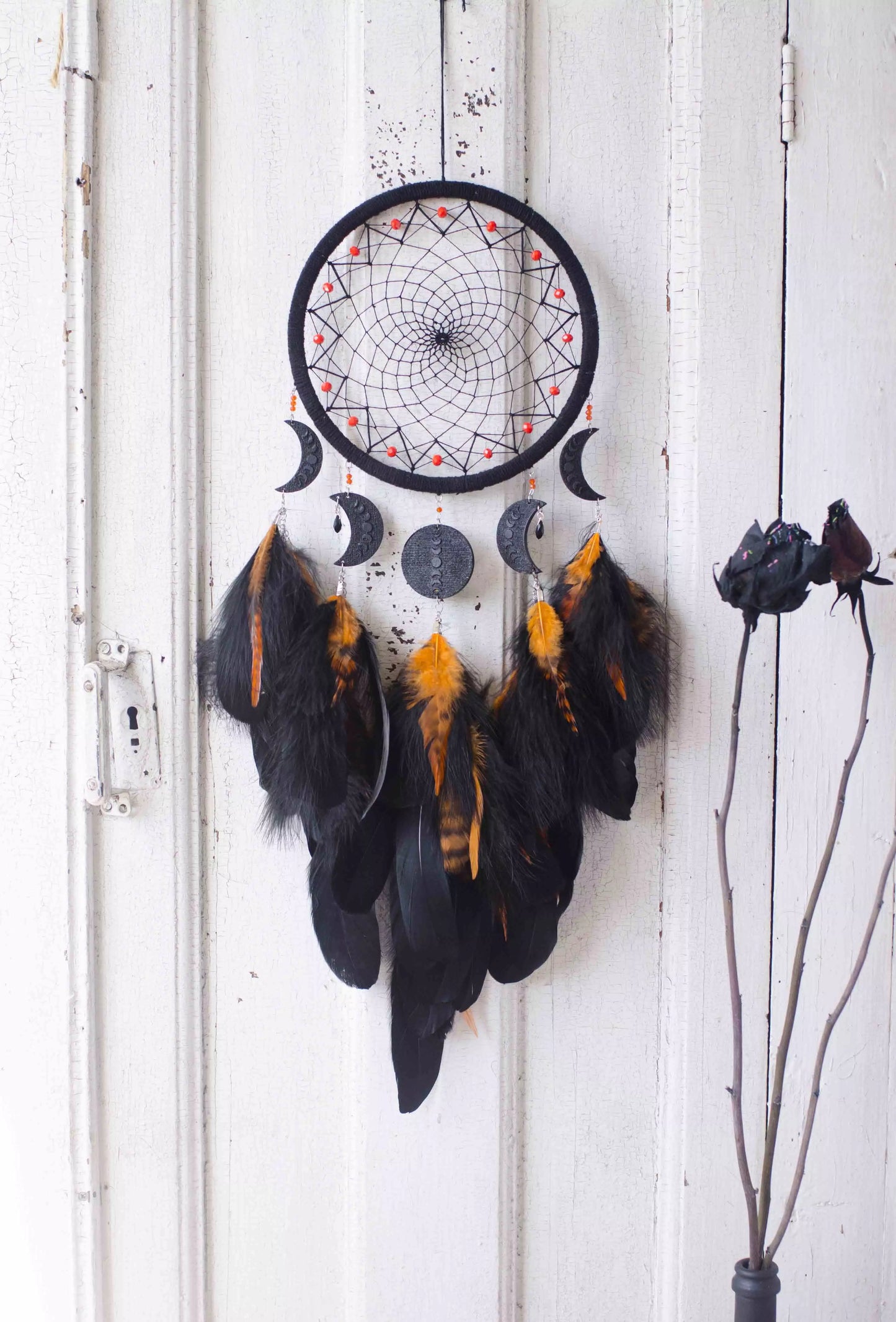 Handcrafted black dream catcher featuring an intricate web design with crescent moon charms and vibrant orange feathers. This bohemian wall decor piece is perfect for capturing negative dreams and channeling positive energy. Ideal for enhancing the aesthetic of any home or office space and makes a thoughtful, spiritual gift.