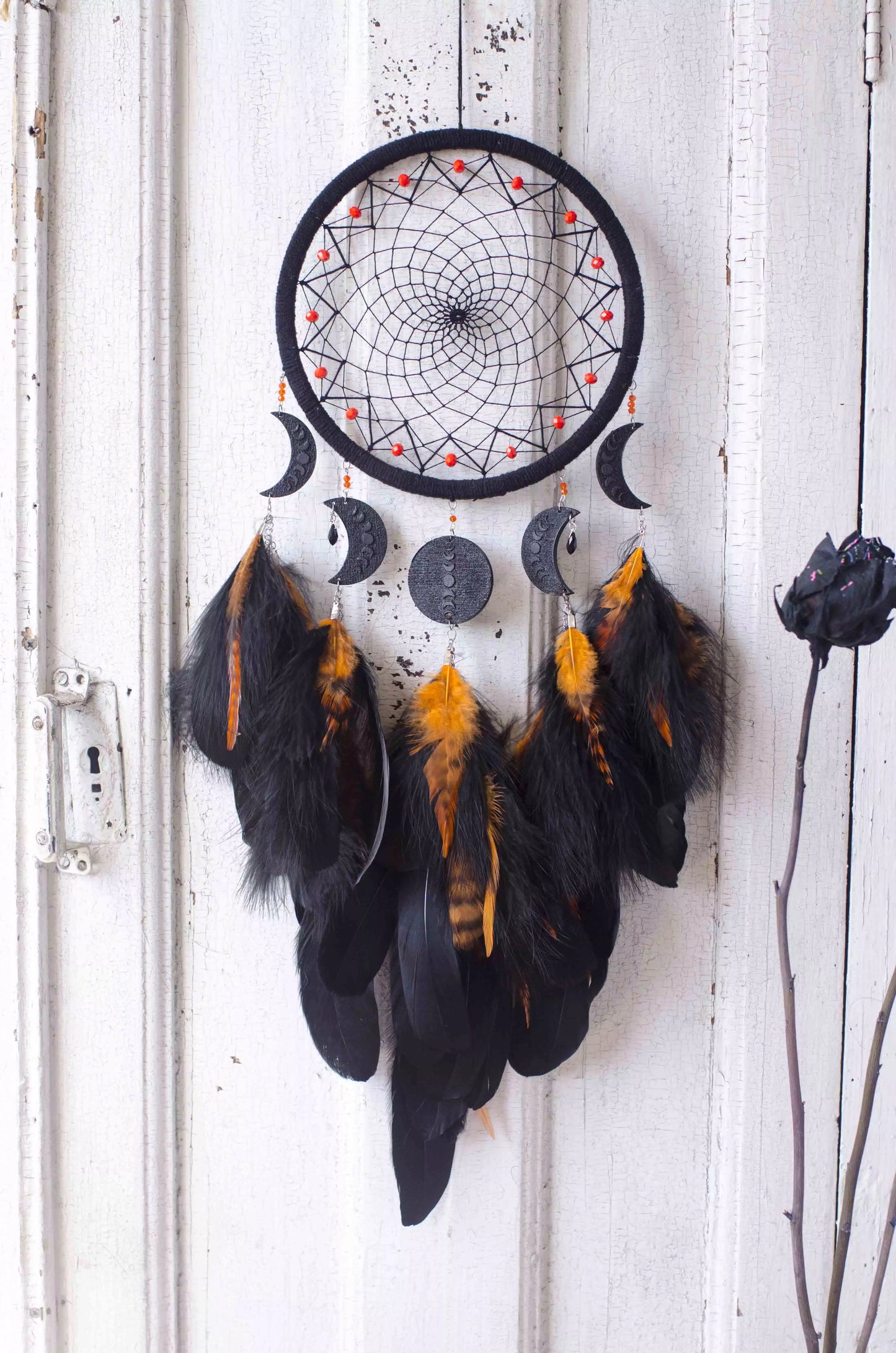Handcrafted black dream catcher featuring an intricate web design with crescent moon charms and vibrant orange feathers. This bohemian wall decor piece is perfect for capturing negative dreams and channeling positive energy. Ideal for enhancing the aesthetic of any home or office space and makes a thoughtful, spiritual gift.
