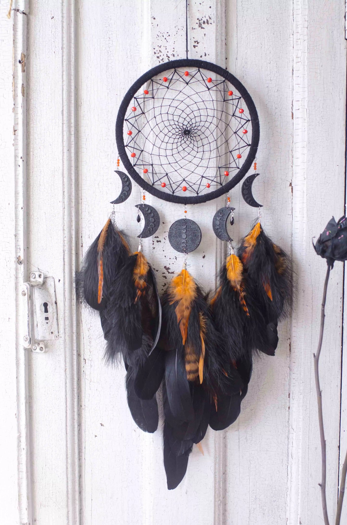 Handcrafted black dream catcher featuring an intricate web design with crescent moon charms and vibrant orange feathers. This bohemian wall decor piece is perfect for capturing negative dreams and channeling positive energy. Ideal for enhancing the aesthetic of any home or office space and makes a thoughtful, spiritual gift.
