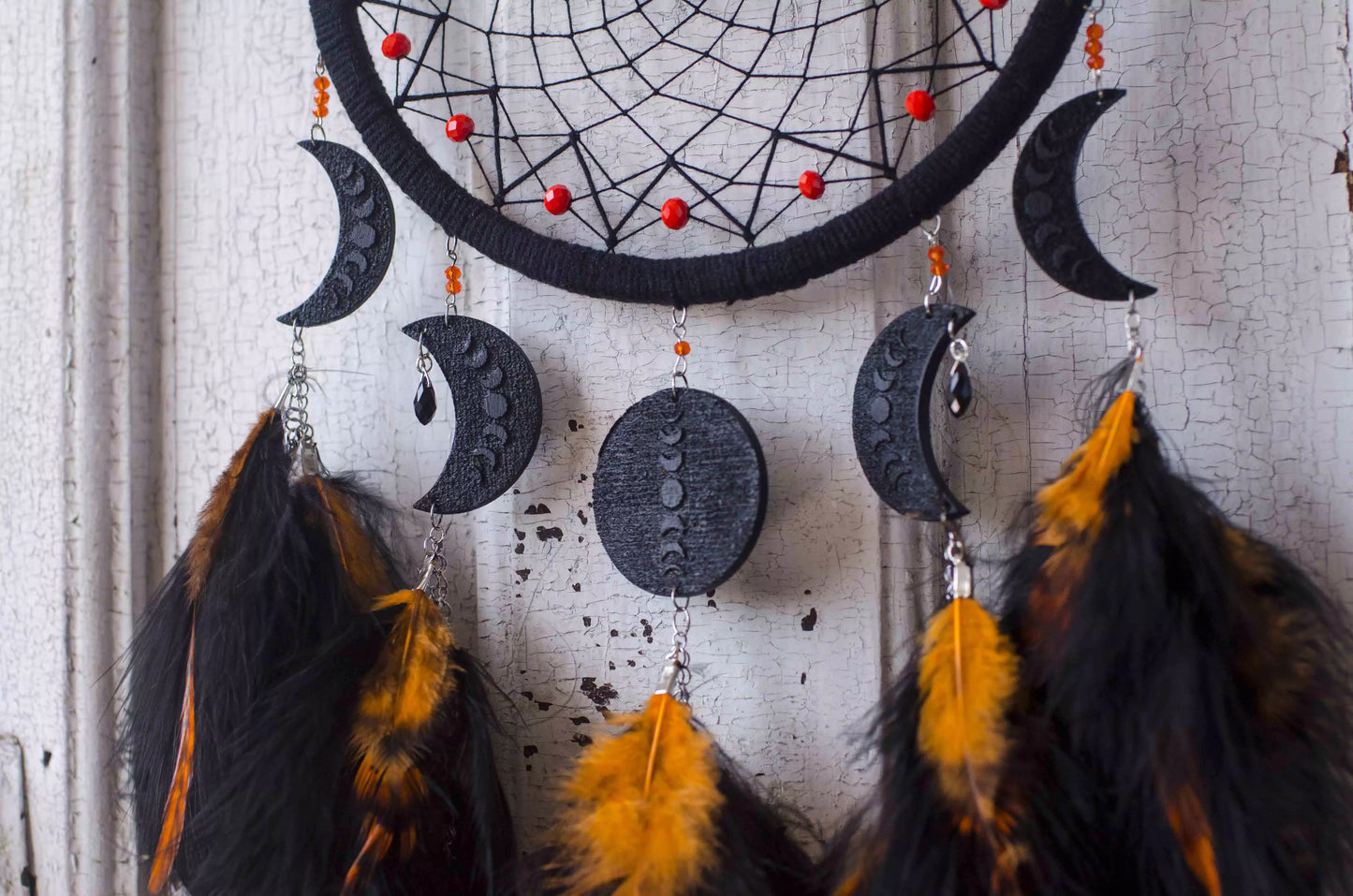 Handcrafted black dream catcher featuring an intricate web design with crescent moon charms and vibrant orange feathers. This bohemian wall decor piece is perfect for capturing negative dreams and channeling positive energy. Ideal for enhancing the aesthetic of any home or office space and makes a thoughtful, spiritual gift.