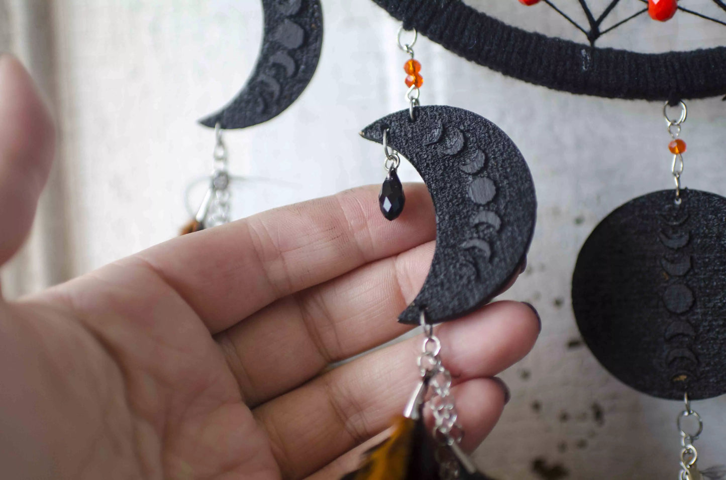 Handcrafted black dream catcher featuring an intricate web design with crescent moon charms and vibrant orange feathers. This bohemian wall decor piece is perfect for capturing negative dreams and channeling positive energy. Ideal for enhancing the aesthetic of any home or office space and makes a thoughtful, spiritual gift.