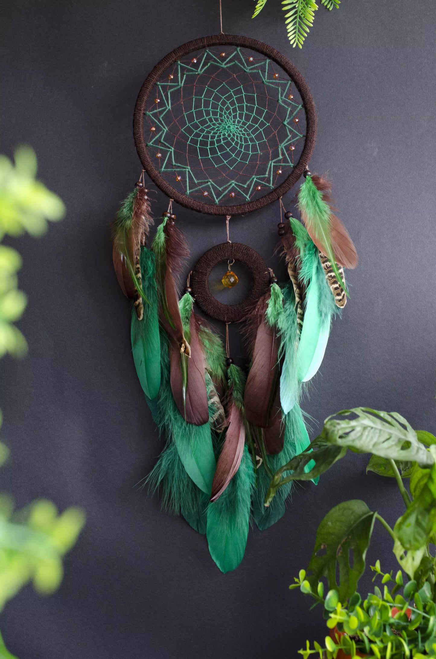 Handcrafted green dream catcher with a faceted amber crystal and natural feathers, featuring an intricate web design and earthy tones. Perfect for home decor or as a spiritual protection gift.