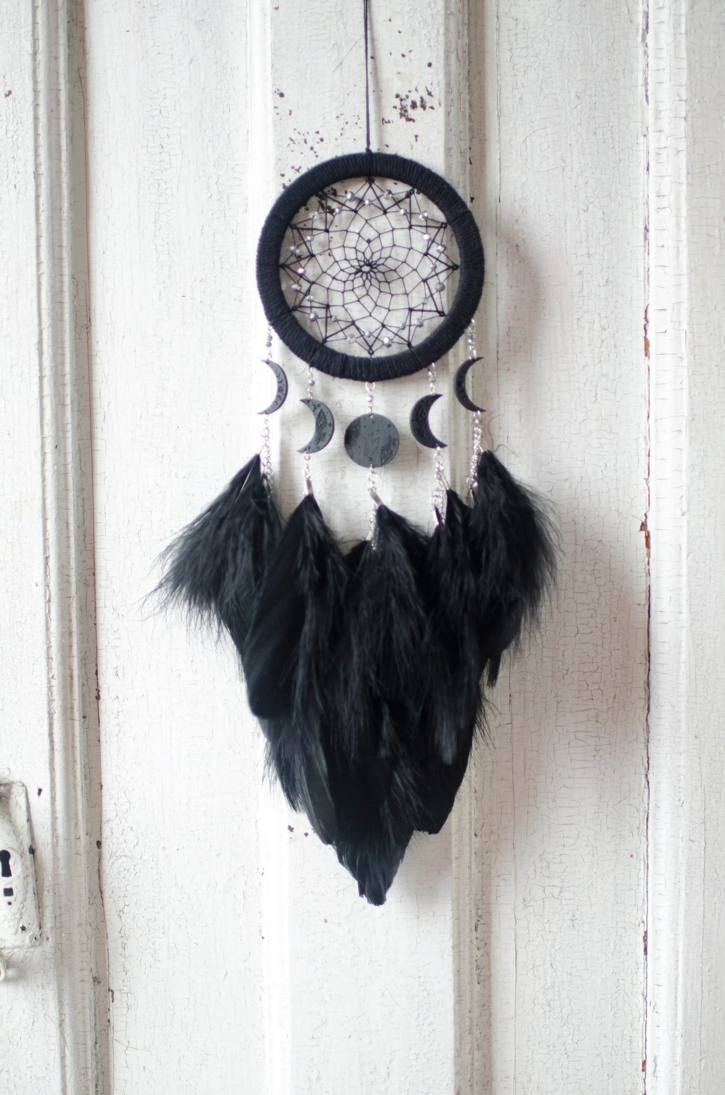 Handcrafted black dream catcher featuring a central web with black beads, adorned with five crescent moons and a central full moon, complemented by lush black feathers.