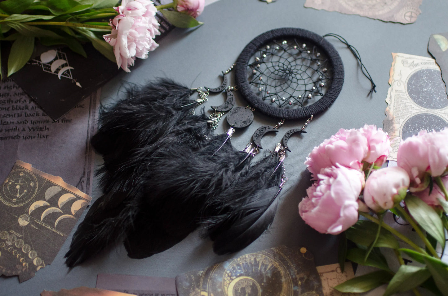 Handcrafted black dream catcher featuring a central web with black beads, adorned with five crescent moons and a central full moon, complemented by lush black feathers.