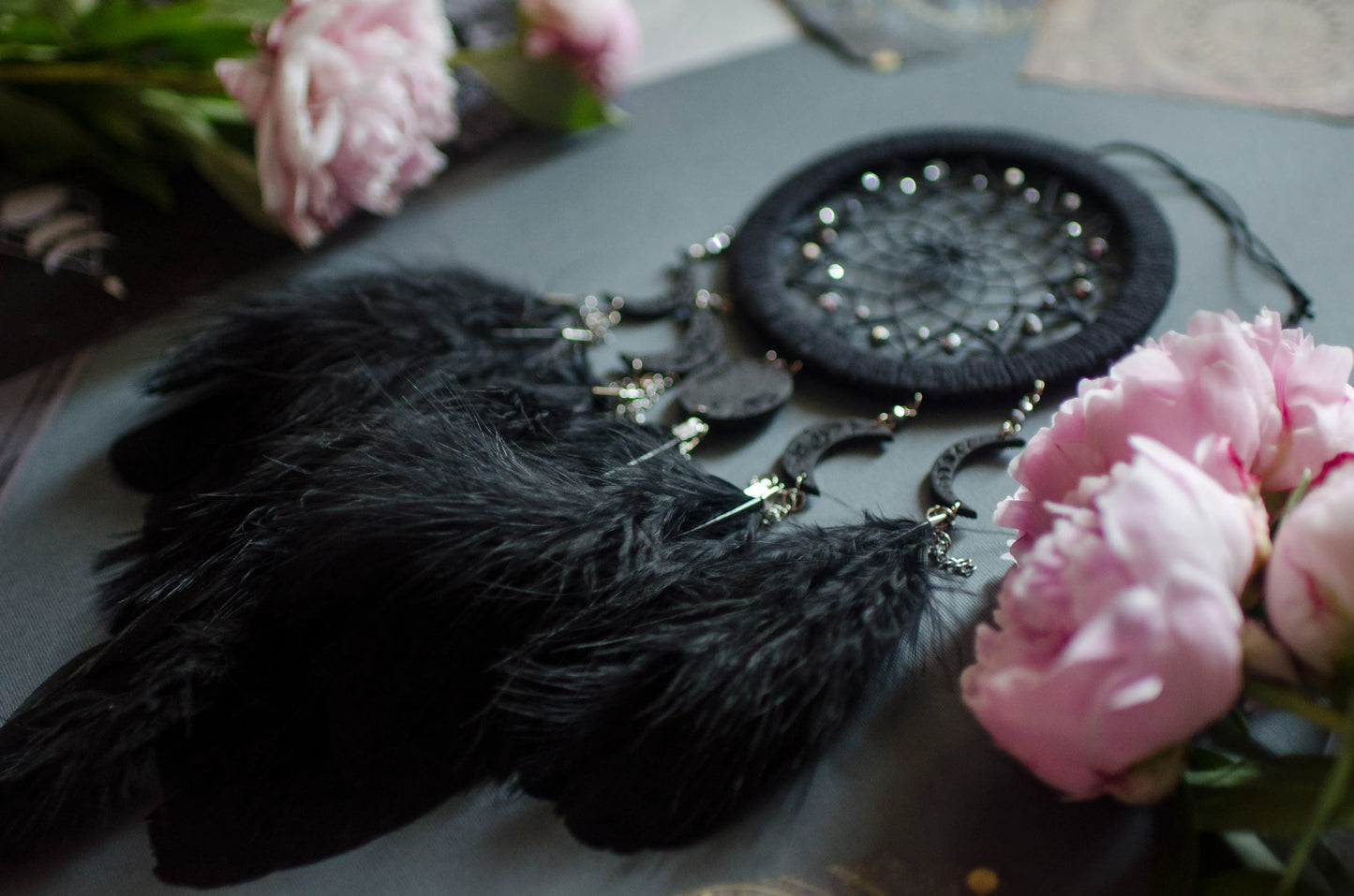 Handcrafted black dream catcher featuring a central web with black beads, adorned with five crescent moons and a central full moon, complemented by lush black feathers.