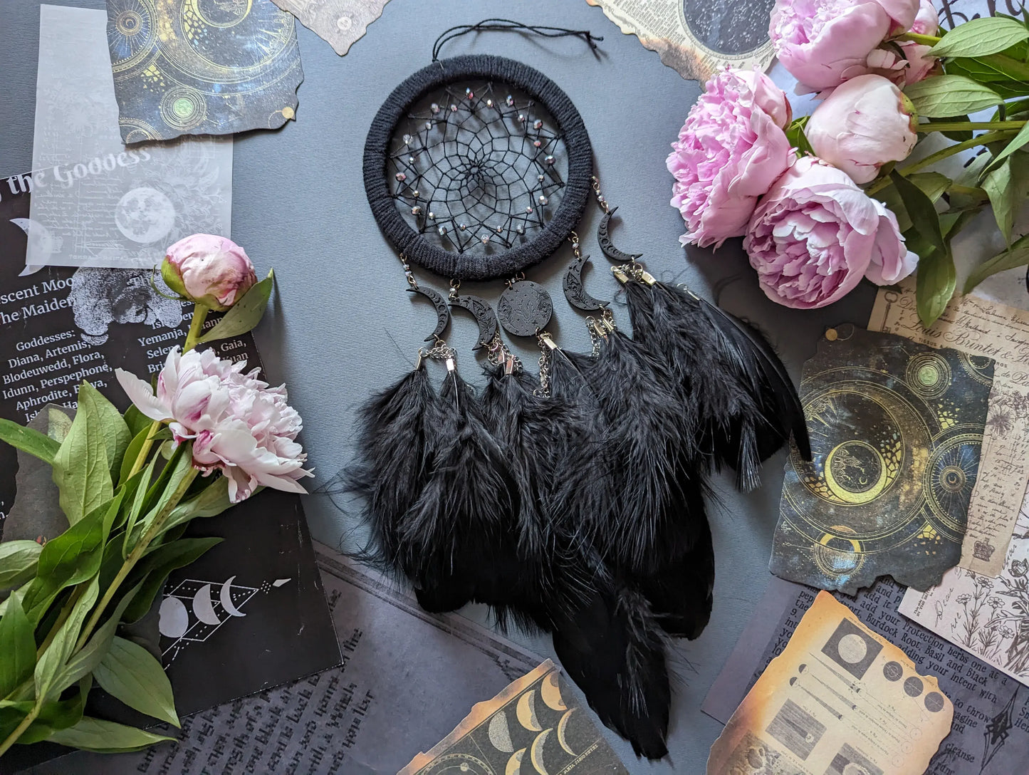 Handcrafted black dream catcher featuring a central web with black beads, adorned with five crescent moons and a central full moon, complemented by lush black feathers.