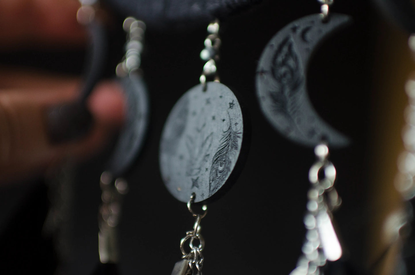 Handcrafted black dream catcher featuring a central web with black beads, adorned with five crescent moons and a central full moon, complemented by lush black feathers.