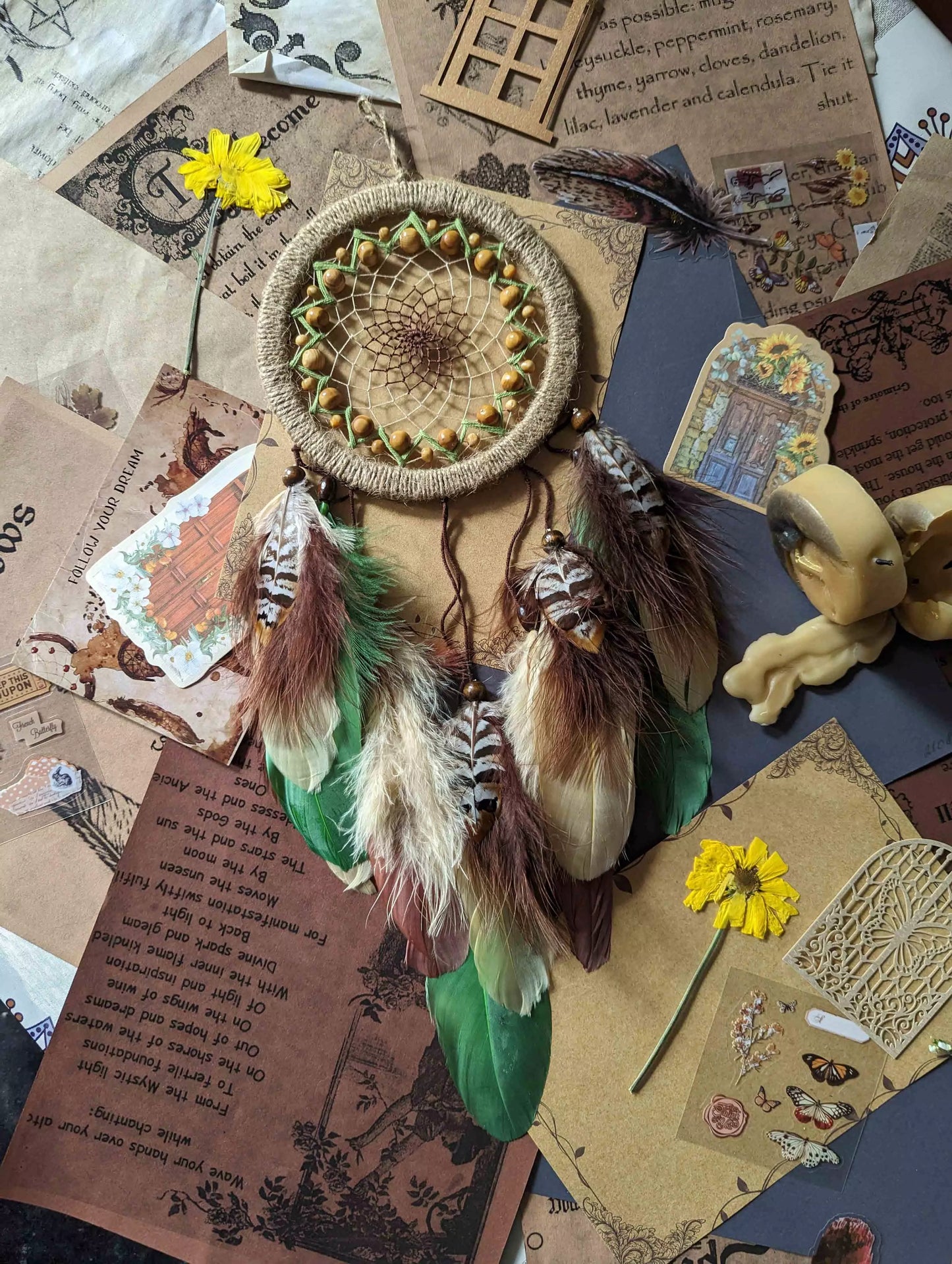 Handmade dream catcher with a 6-inch hoop wrapped in natural jute twine, featuring an intricate web design with wooden beads. Adorned with an array of feathers in green, cream, and brown tones, it serves as a beautiful boho wall decor piece. Perfect for adding a touch of rustic charm to any room.