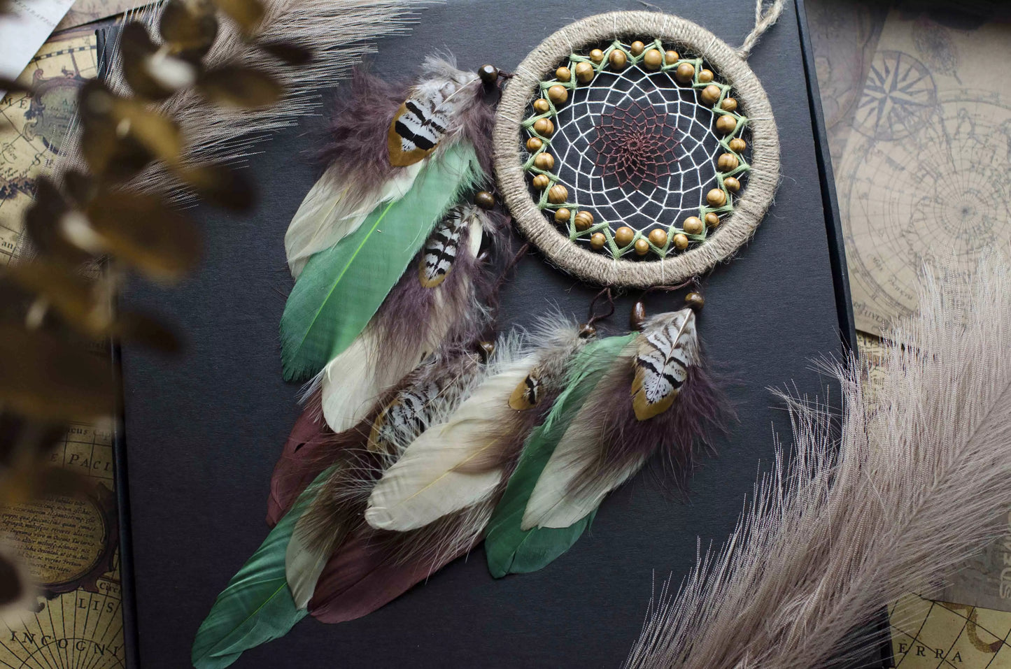 Handmade dream catcher with a 6-inch hoop wrapped in natural jute twine, featuring an intricate web design with wooden beads. Adorned with an array of feathers in green, cream, and brown tones, it serves as a beautiful boho wall decor piece. Perfect for adding a touch of rustic charm to any room.