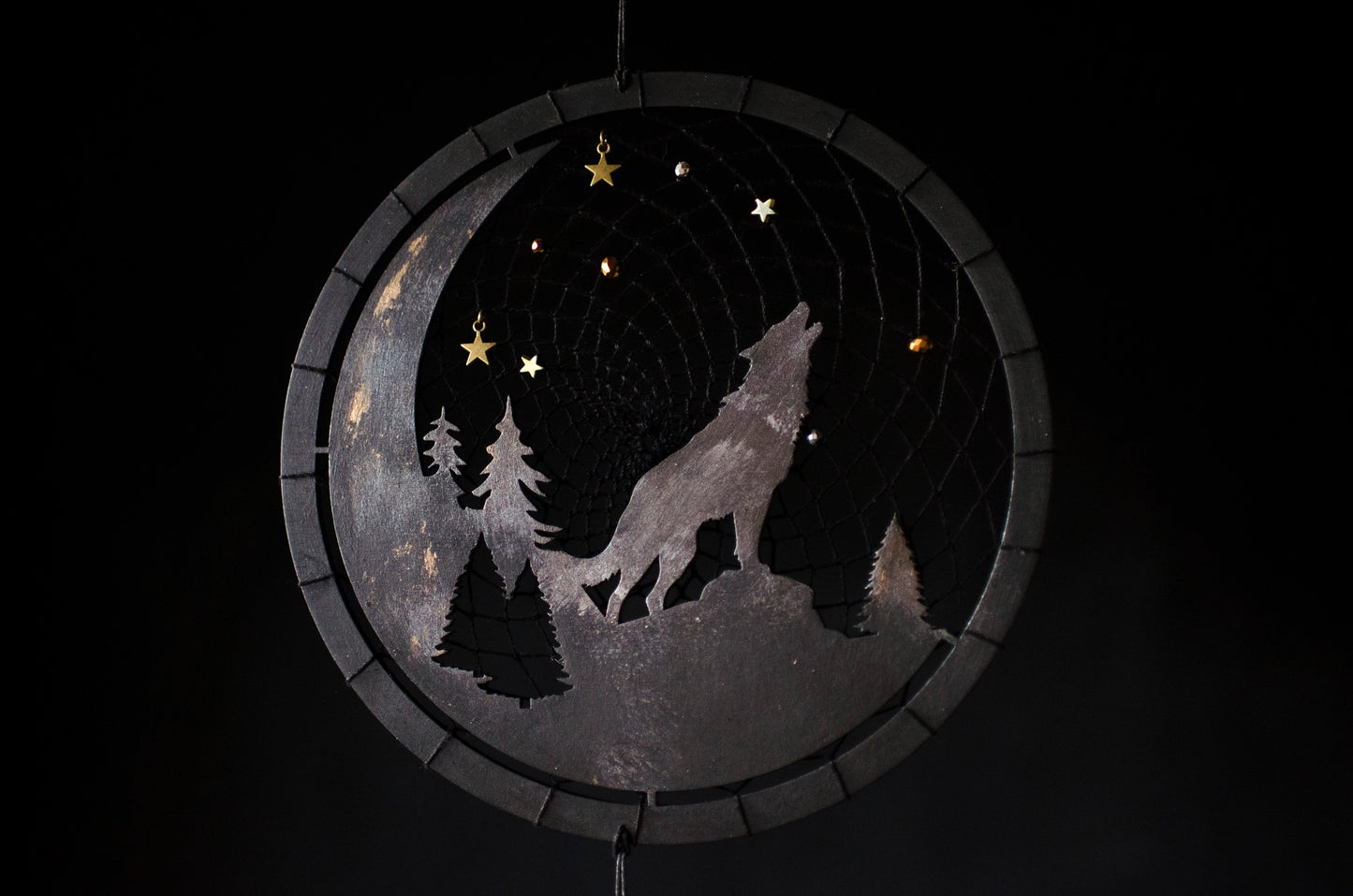 A handcrafted dream catcher with a howling wolf silhouette, moon, and forest design. Decorated with star-shaped beads, this unique piece captures the essence of the night. The hoop measures approximately 8 inches in diameter, featuring black and natural shades.