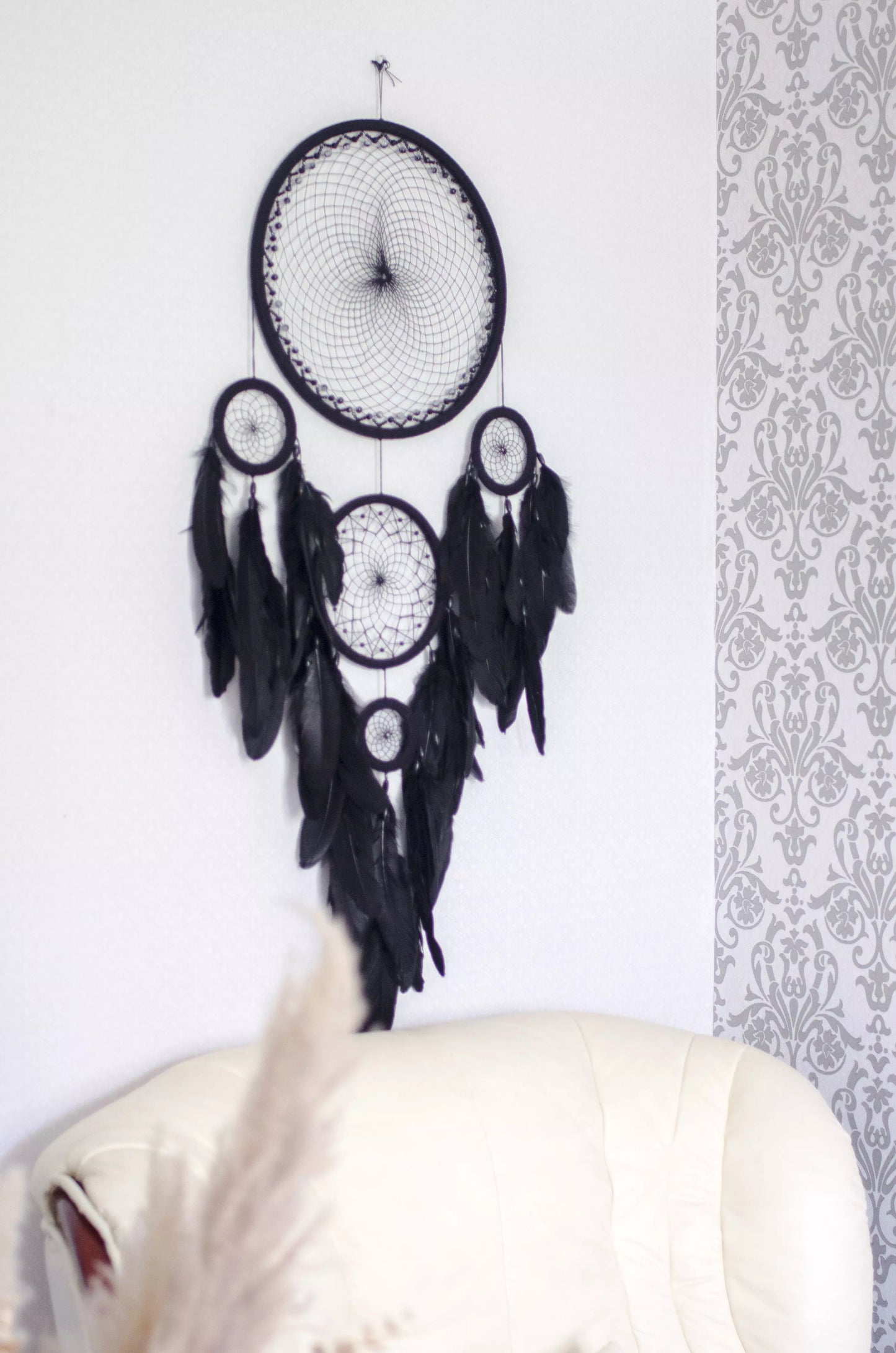 Large black multi-ring dreamcatcher featuring intricate woven web and cascading black feathers. Handcrafted boho and gothic wall decor, perfect for adding a statement piece to bedrooms or living rooms. Measures approximately 40 inches in height.