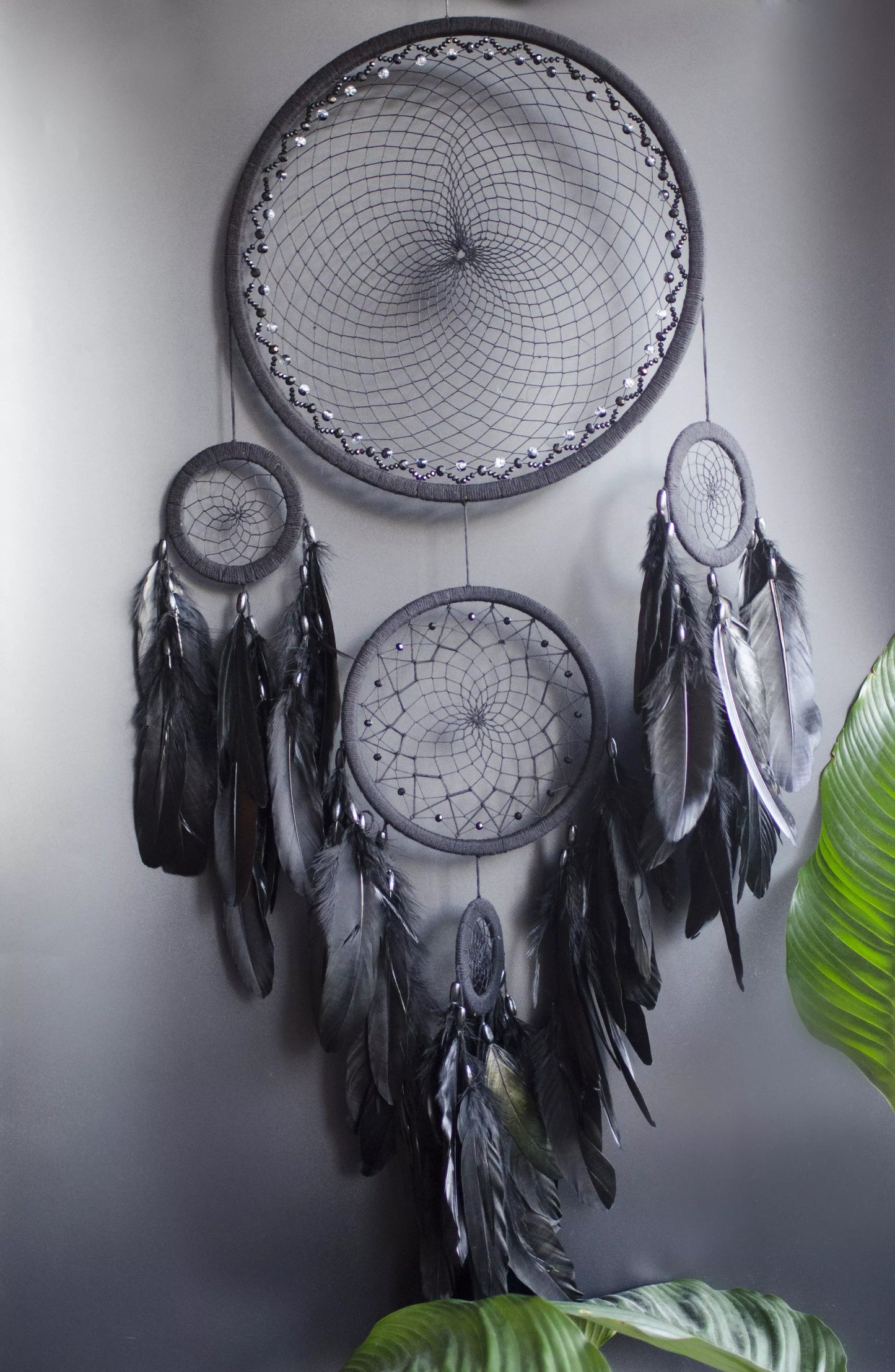 Large black multi-ring dreamcatcher featuring intricate woven web and cascading black feathers. Handcrafted boho and gothic wall decor, perfect for adding a statement piece to bedrooms or living rooms. Measures approximately 40 inches in height.