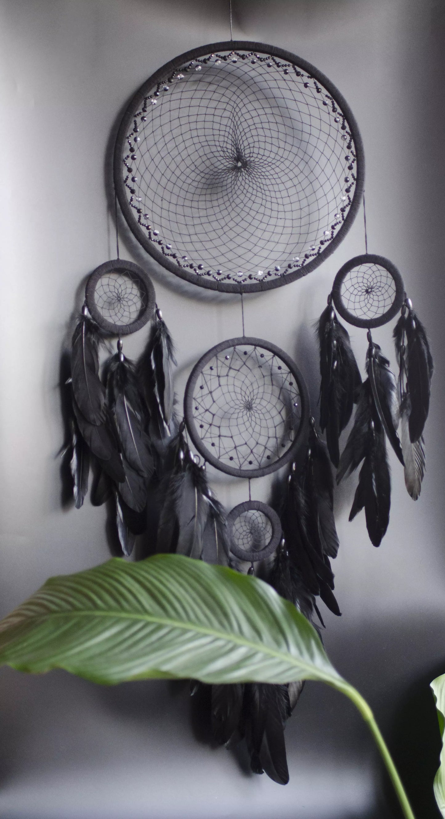 Large black multi-ring dreamcatcher featuring intricate woven web and cascading black feathers. Handcrafted boho and gothic wall decor, perfect for adding a statement piece to bedrooms or living rooms. Measures approximately 40 inches in height.