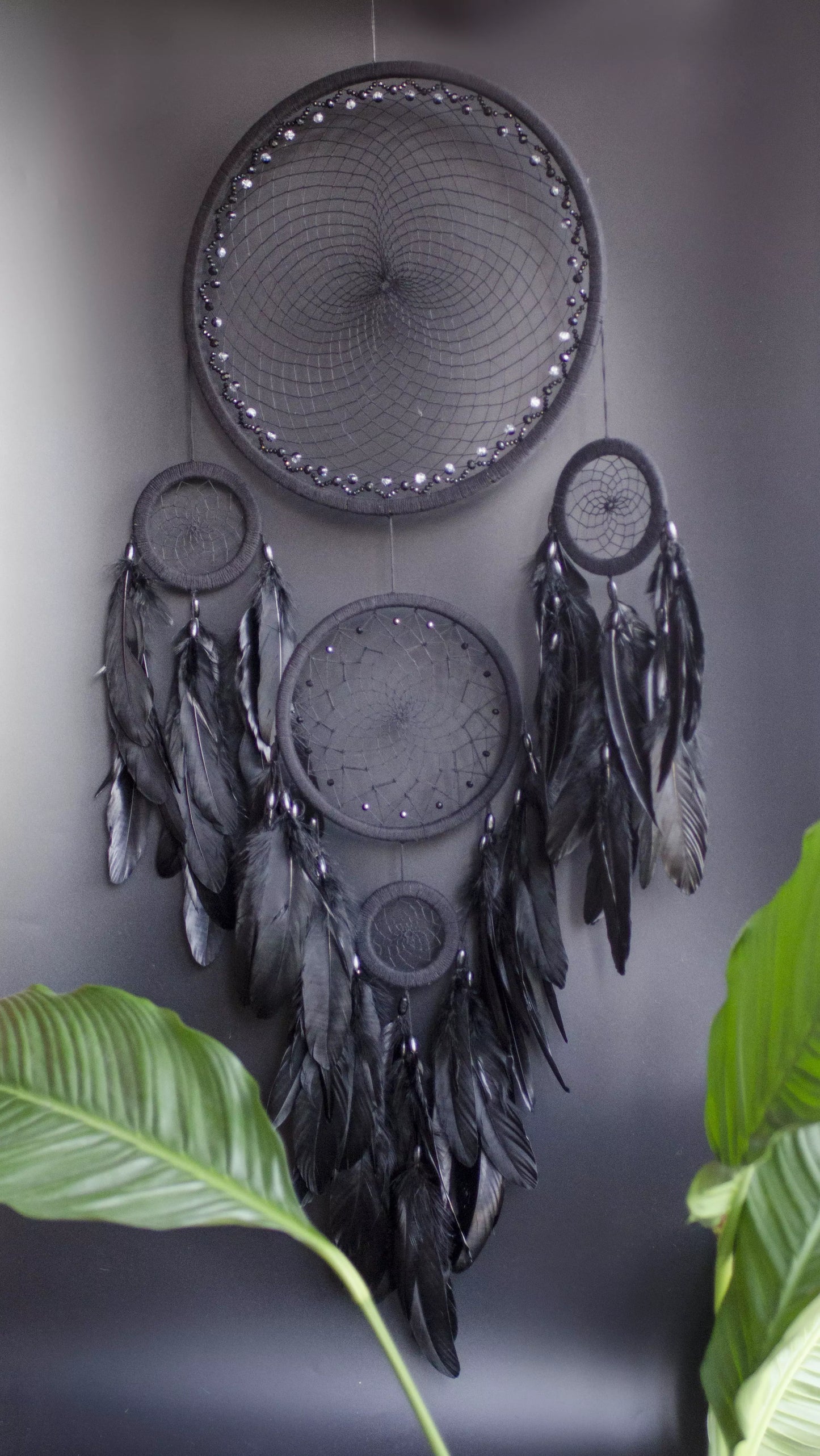 Large black multi-ring dreamcatcher featuring intricate woven web and cascading black feathers. Handcrafted boho and gothic wall decor, perfect for adding a statement piece to bedrooms or living rooms. Measures approximately 40 inches in height.