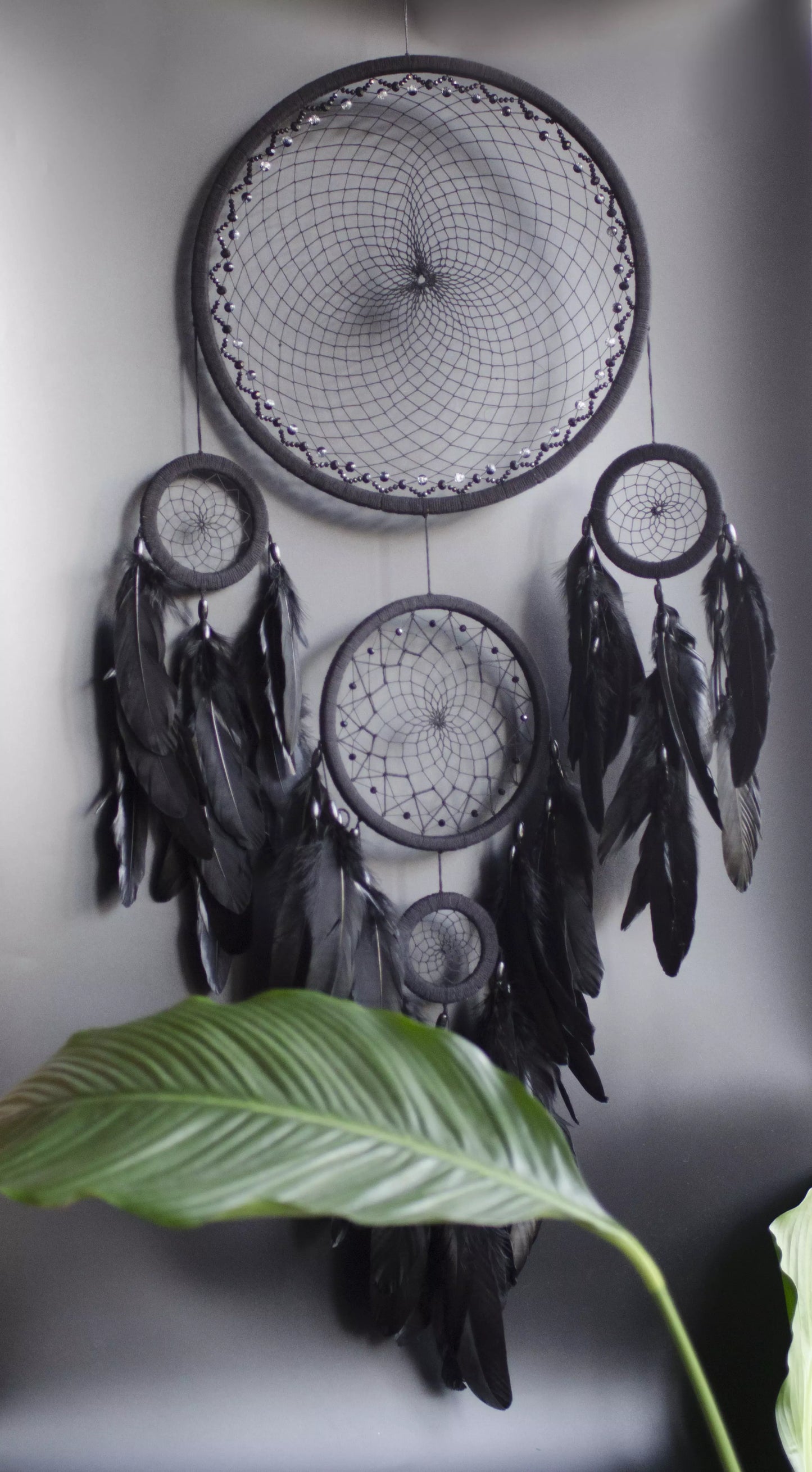 Large black multi-ring dreamcatcher featuring intricate woven web and cascading black feathers. Handcrafted boho and gothic wall decor, perfect for adding a statement piece to bedrooms or living rooms. Measures approximately 40 inches in height.