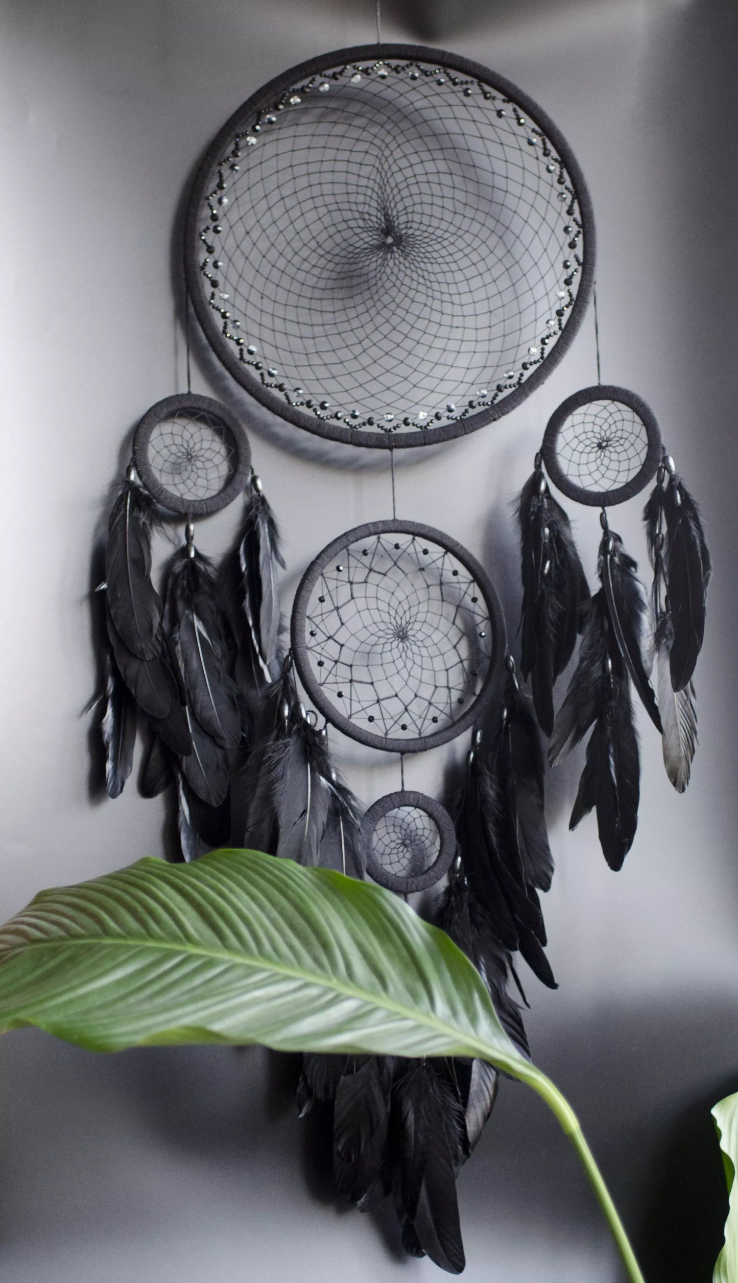 Large black multi-ring dreamcatcher featuring intricate woven web and cascading black feathers. Handcrafted boho and gothic wall decor, perfect for adding a statement piece to bedrooms or living rooms. Measures approximately 40 inches in height.