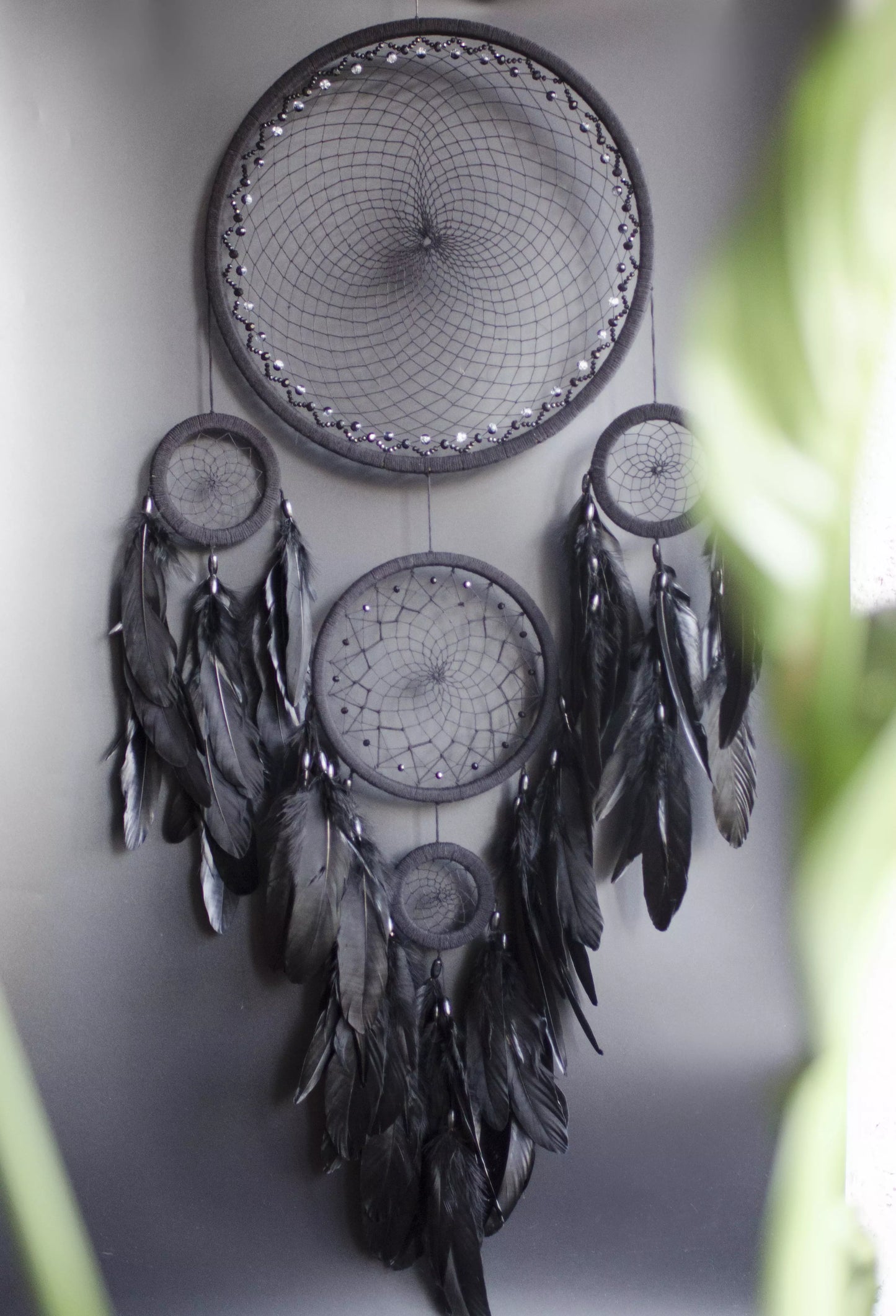 Large black multi-ring dreamcatcher featuring intricate woven web and cascading black feathers. Handcrafted boho and gothic wall decor, perfect for adding a statement piece to bedrooms or living rooms. Measures approximately 40 inches in height.