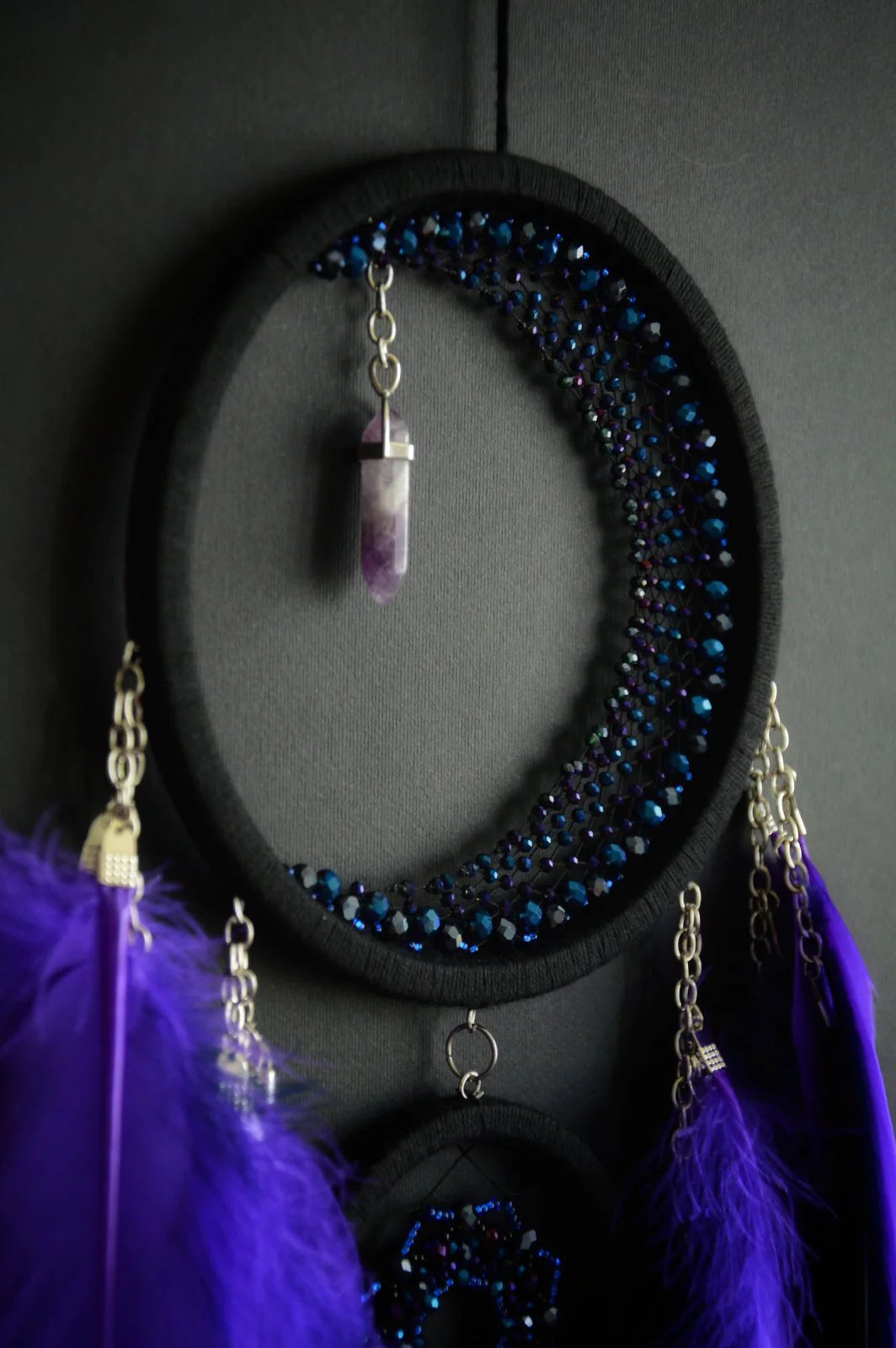 Handmade purple crescent moon dreamcatcher with black hoop, amethyst crystal, and purple-black feathers. Boho wall hanging with calming energy and spiritual symbolism.