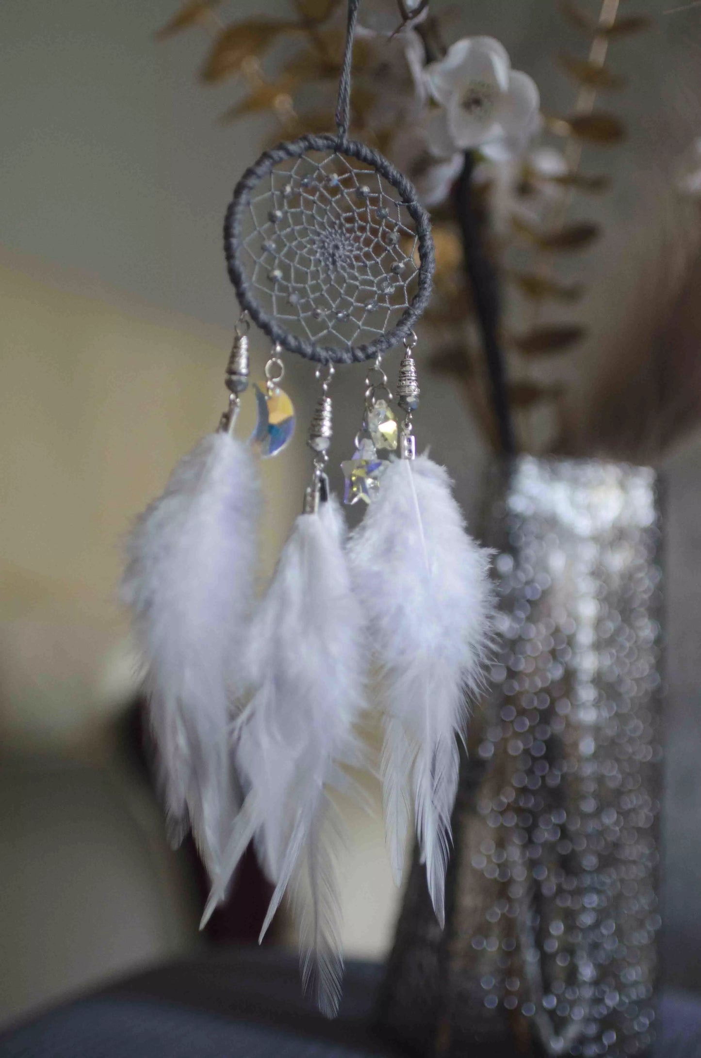 Handmade gray dreamcatcher with dark gray hoop, intricate web adorned with sparkling beads and shimmering crystals, and soft white feathers. Compact size ideal for car rearview mirror or home decor, offering a serene, bohemian aesthetic.