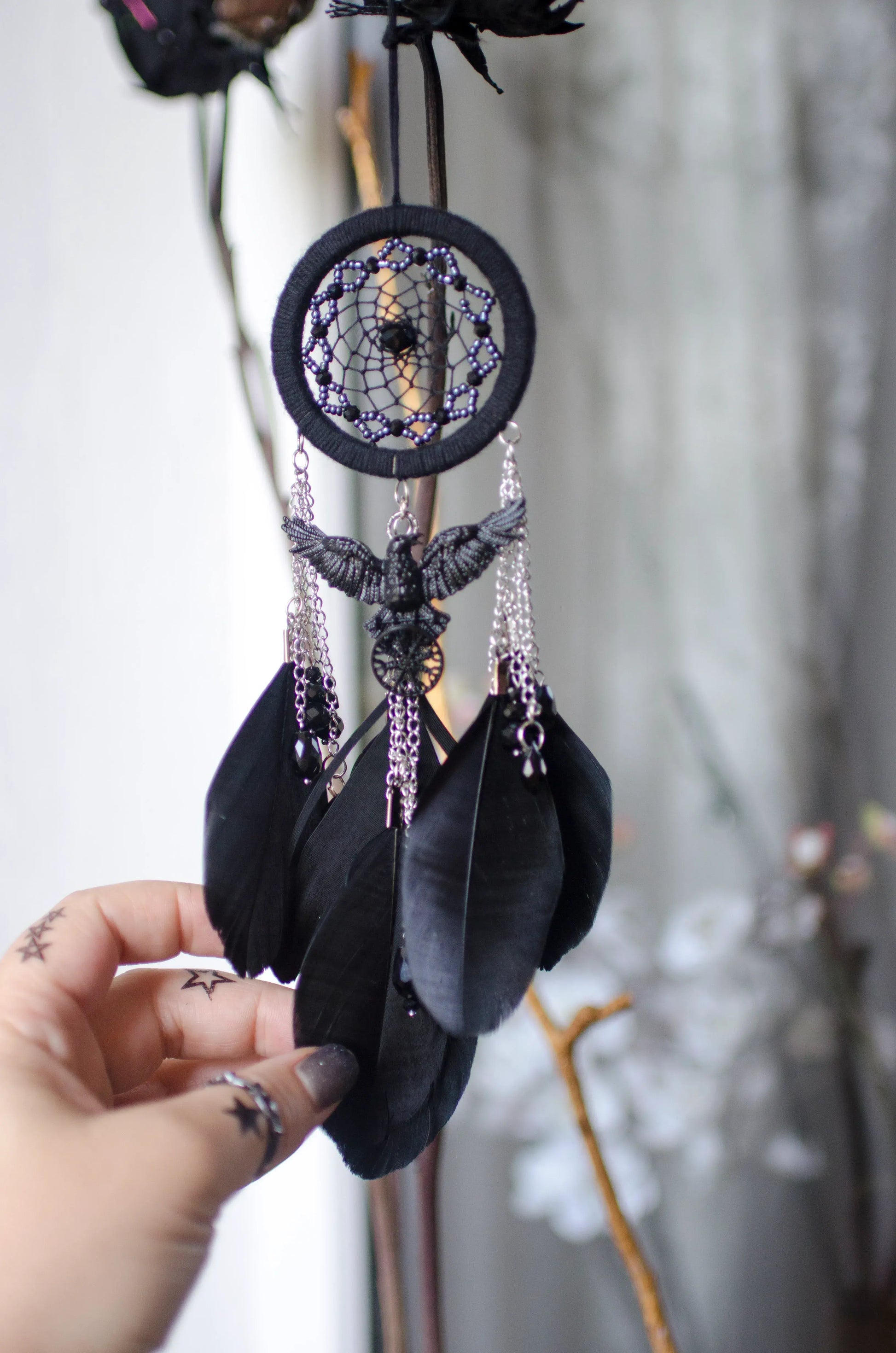 Handcrafted mini dream catcher with a black hoop and web adorned with purple beads, featuring a central raven charm with purple chains and black feathers. Ideal for gothic or bohemian decor.