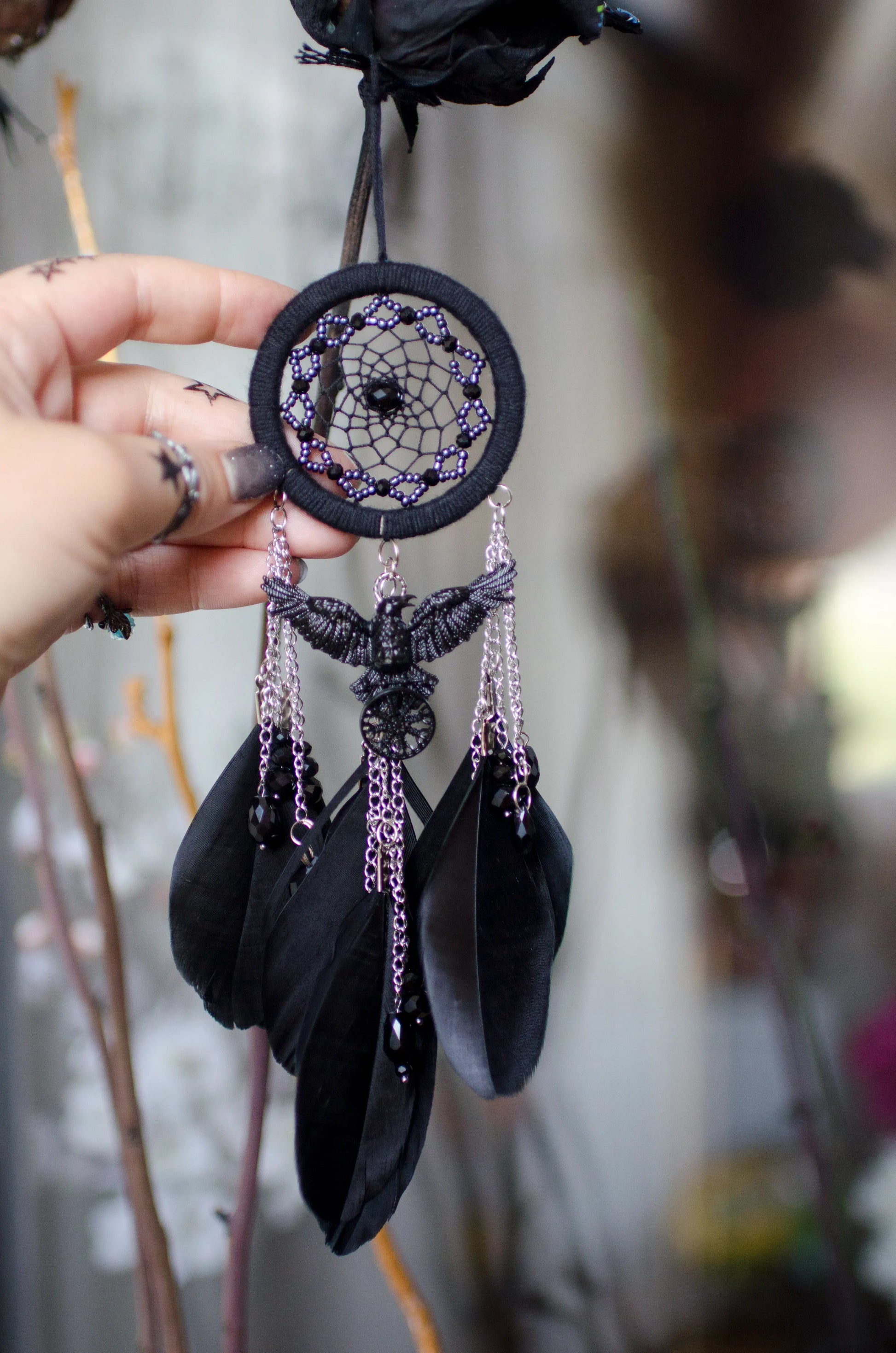 Handcrafted mini dream catcher with a black hoop and web adorned with purple beads, featuring a central raven charm with purple chains and black feathers. Ideal for gothic or bohemian decor.