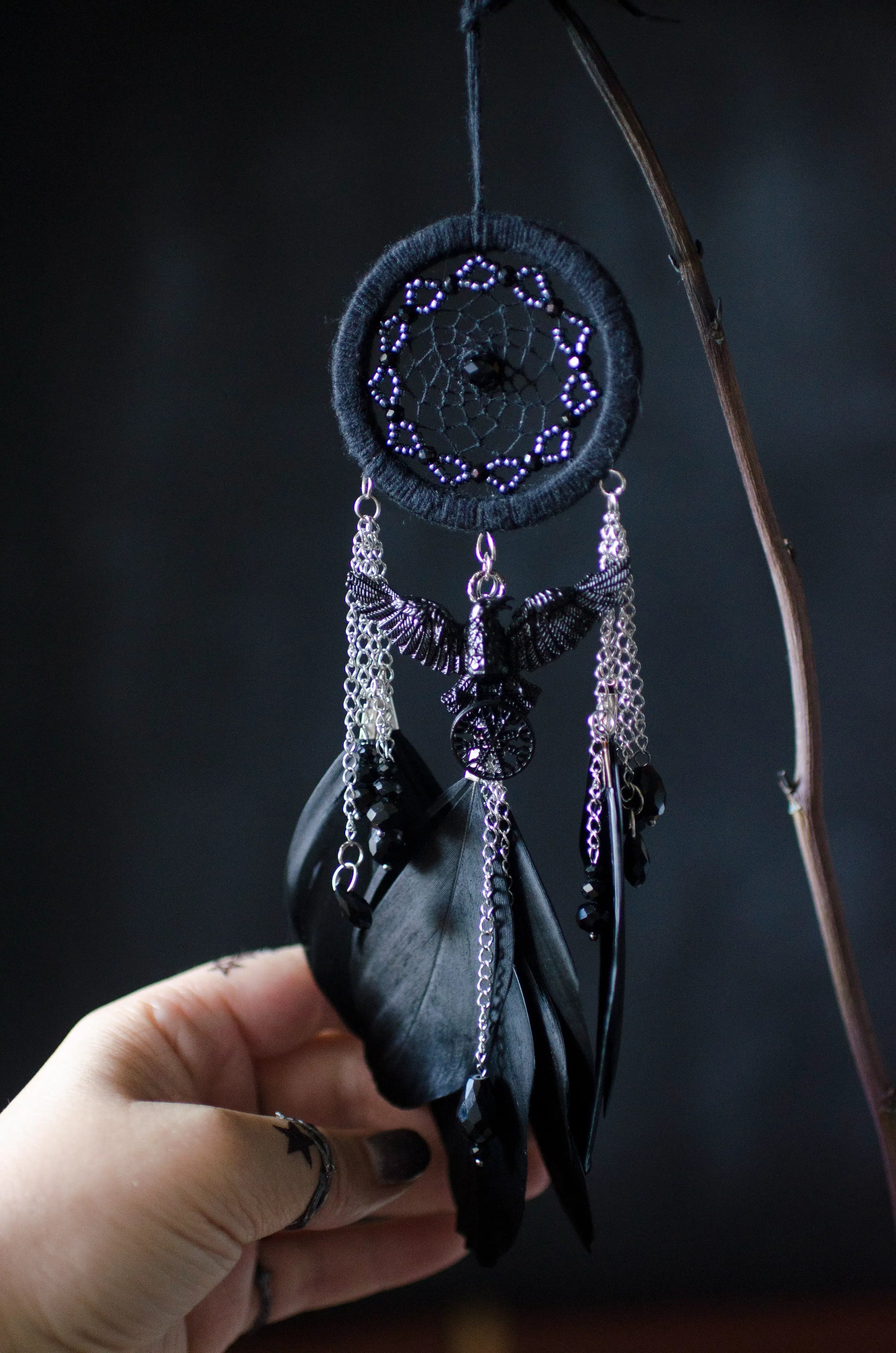 Handcrafted mini dream catcher with a black hoop and web adorned with purple beads, featuring a central raven charm with purple chains and black feathers. Ideal for gothic or bohemian decor.