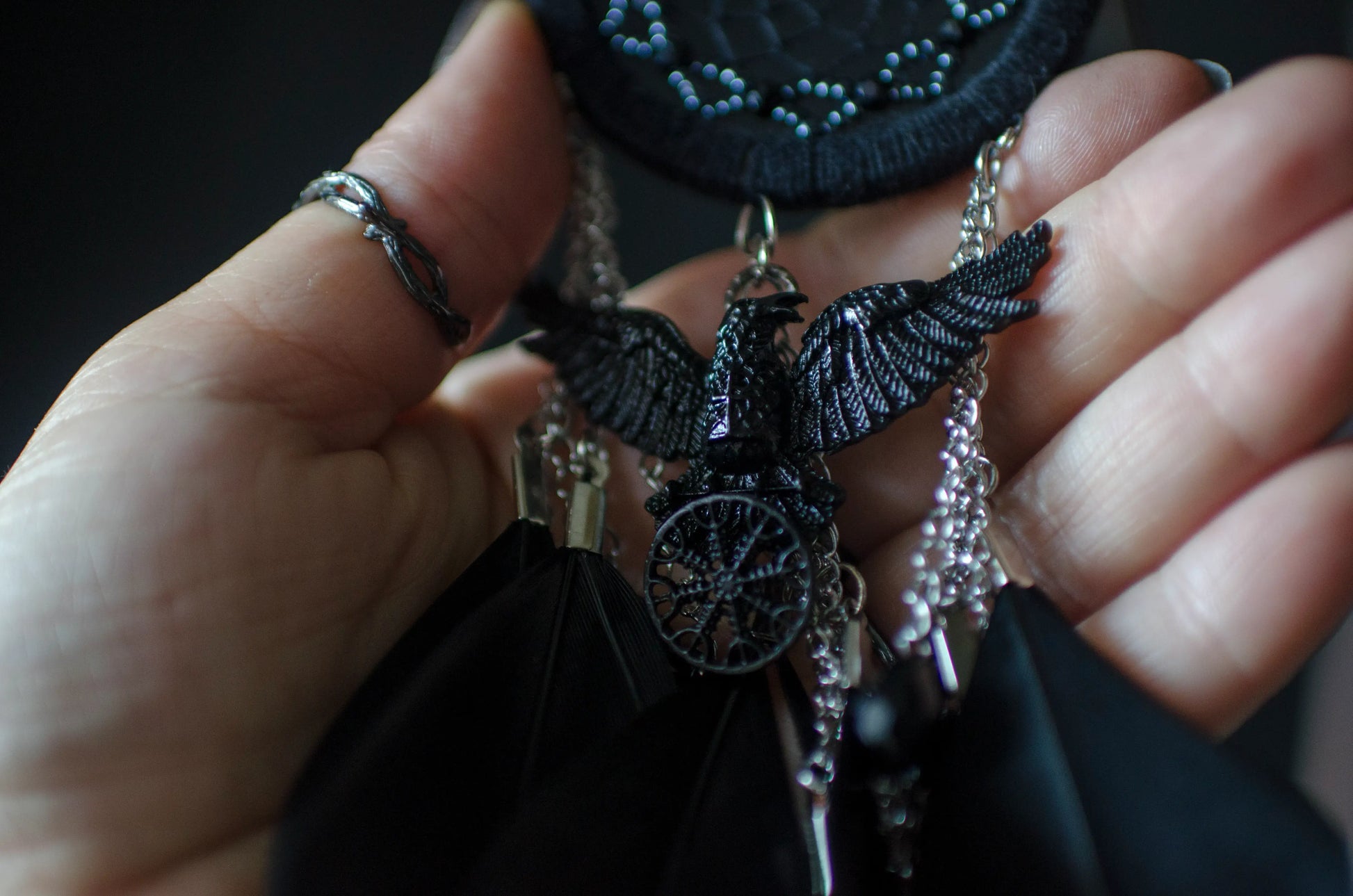 Handcrafted mini dream catcher with a black hoop and web adorned with purple beads, featuring a central raven charm with purple chains and black feathers. Ideal for gothic or bohemian decor.