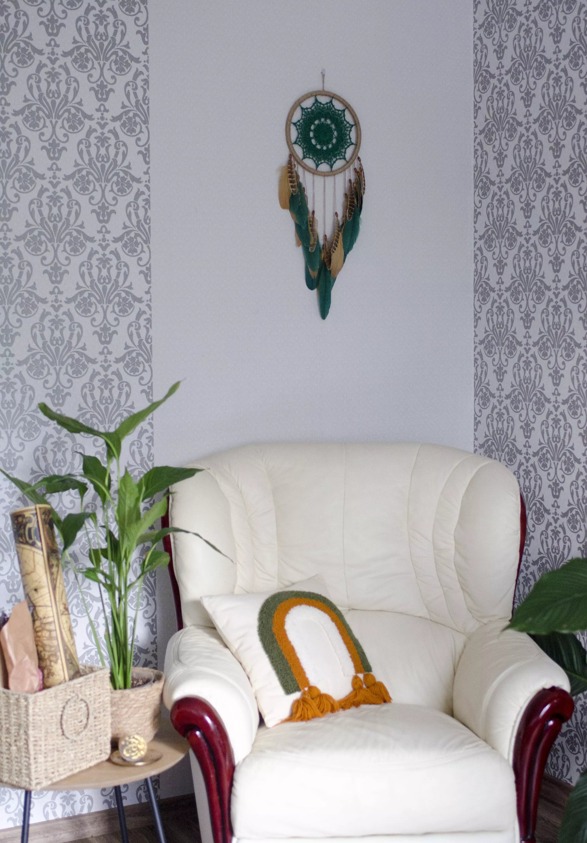 A handcrafted dreamcatcher featuring a green crochet mandala centerpiece, wrapped in a jute hoop with natural brown and green feathers hanging below, styled against dark and light backgrounds for a modern, bohemian look.