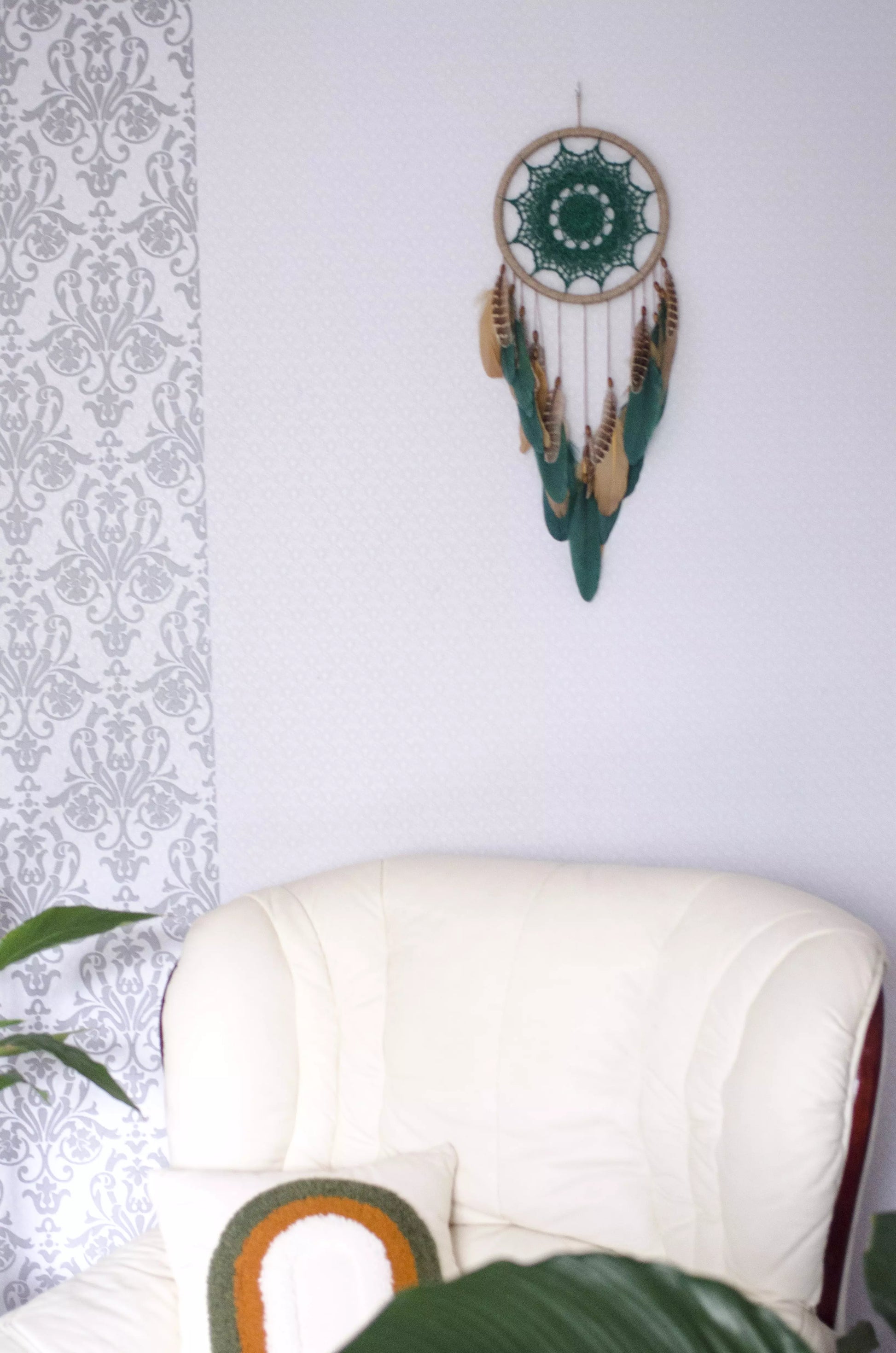 A handcrafted dreamcatcher featuring a green crochet mandala centerpiece, wrapped in a jute hoop with natural brown and green feathers hanging below, styled against dark and light backgrounds for a modern, bohemian look.