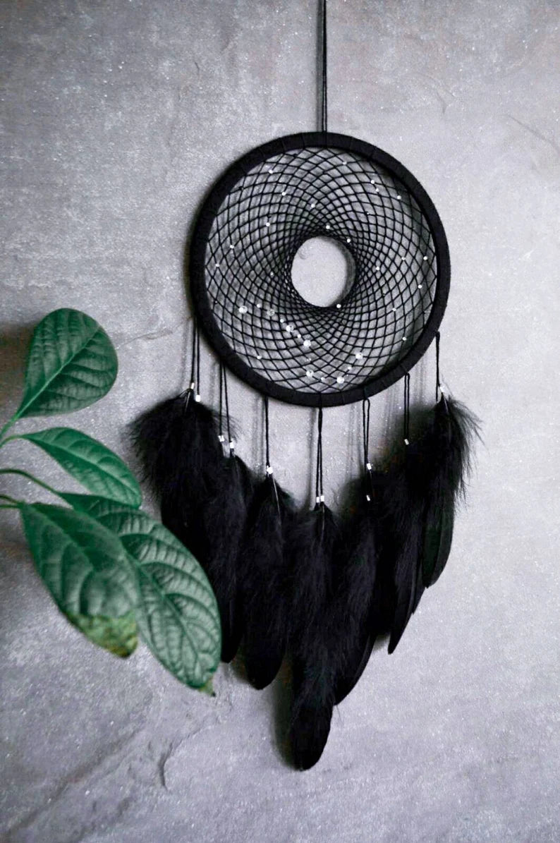 Handmade dreamcatcher with a black hoop, featuring a meticulously woven web adorned with small reflective beads, creating a galaxy-like effect. The dreamcatcher is embellished with vibrant blue and purple feathers, adding a striking contrast and visual appeal. Perfect for adding a touch of mystique and elegance to any space.