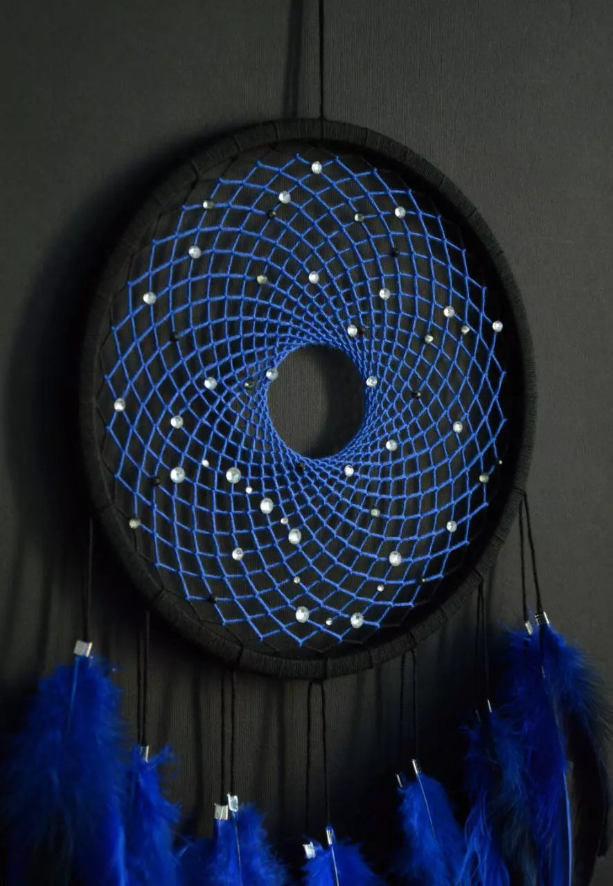 Handmade dreamcatcher with a black hoop, featuring a meticulously woven web adorned with small reflective beads, creating a galaxy-like effect. The dreamcatcher is embellished with vibrant blue and purple feathers, adding a striking contrast and visual appeal. Perfect for adding a touch of mystique and elegance to any space.