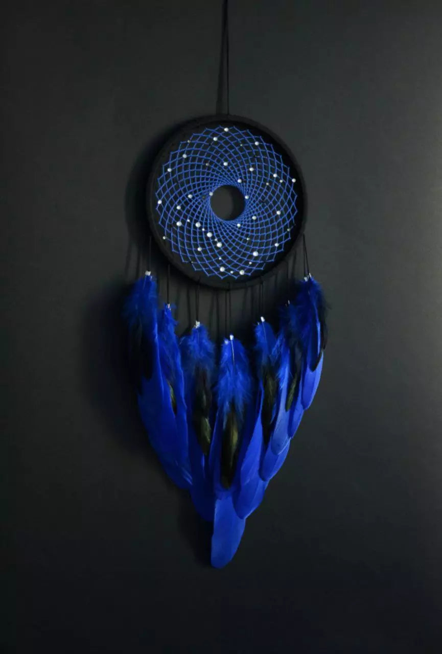 Handmade dreamcatcher with a black hoop, featuring a meticulously woven web adorned with small reflective beads, creating a galaxy-like effect. The dreamcatcher is embellished with vibrant blue and purple feathers, adding a striking contrast and visual appeal. Perfect for adding a touch of mystique and elegance to any space.