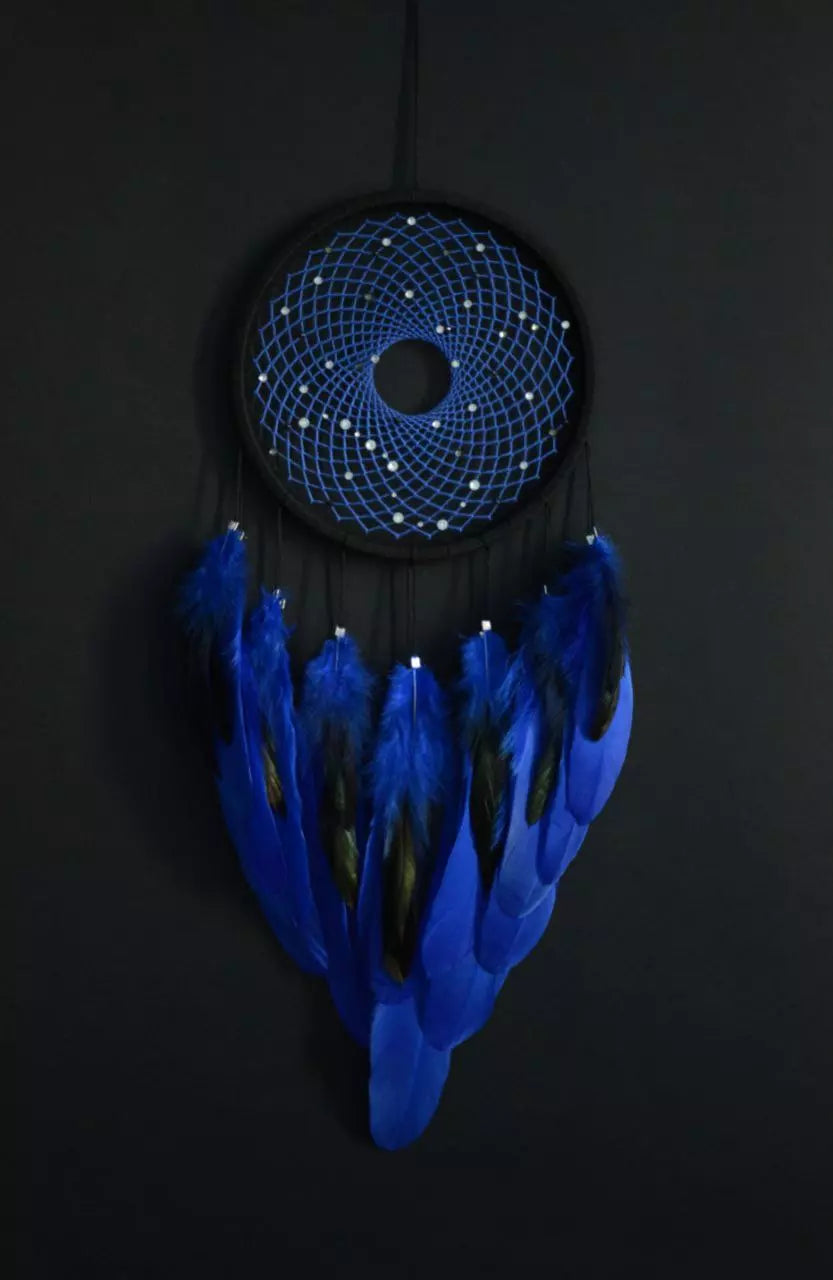 Handmade dreamcatcher with a black hoop, featuring a meticulously woven web adorned with small reflective beads, creating a galaxy-like effect. The dreamcatcher is embellished with vibrant blue and purple feathers, adding a striking contrast and visual appeal. Perfect for adding a touch of mystique and elegance to any space.