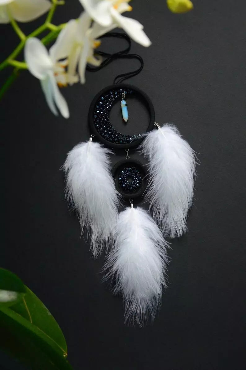 Handmade crescent moon dreamcatcher with white feathers, black aventurine crystals, and a moonstone pendant, designed for boho decor, spiritual protection, and a mystical ambiance.