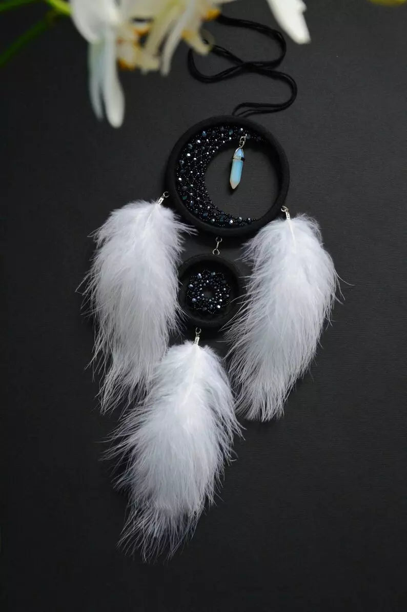 Handmade crescent moon dreamcatcher with white feathers, black aventurine crystals, and a moonstone pendant, designed for boho decor, spiritual protection, and a mystical ambiance.