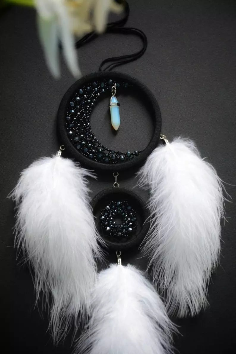 Handmade crescent moon dreamcatcher with white feathers, black aventurine crystals, and a moonstone pendant, designed for boho decor, spiritual protection, and a mystical ambiance.