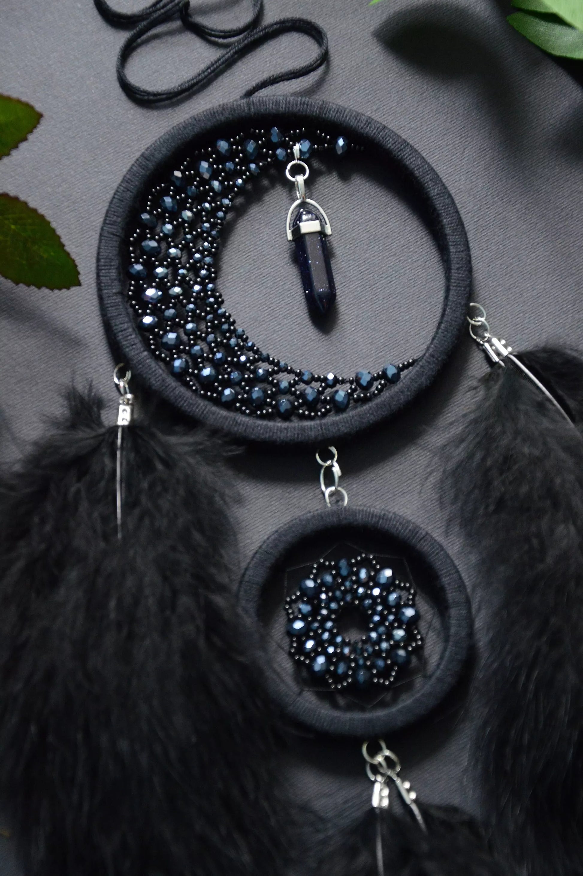 Handmade black crescent moon dreamcatcher adorned with black aventurine crystals, black beads, and soft black feathers, designed for boho and gothic decor, spiritual protection, and mystical ambiance in any space.