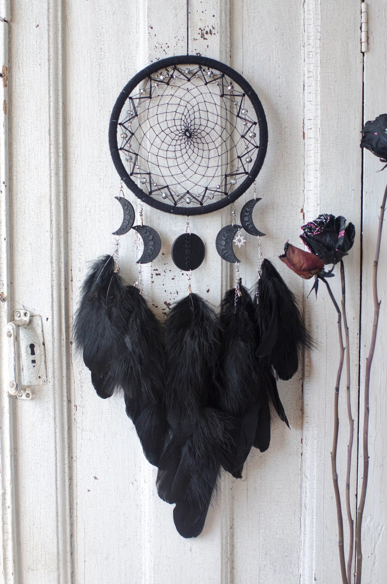 Handcrafted black dream catcher featuring a central web with black beads, adorned with five crescent moons and a central full moon, complemented by lush black feathers.