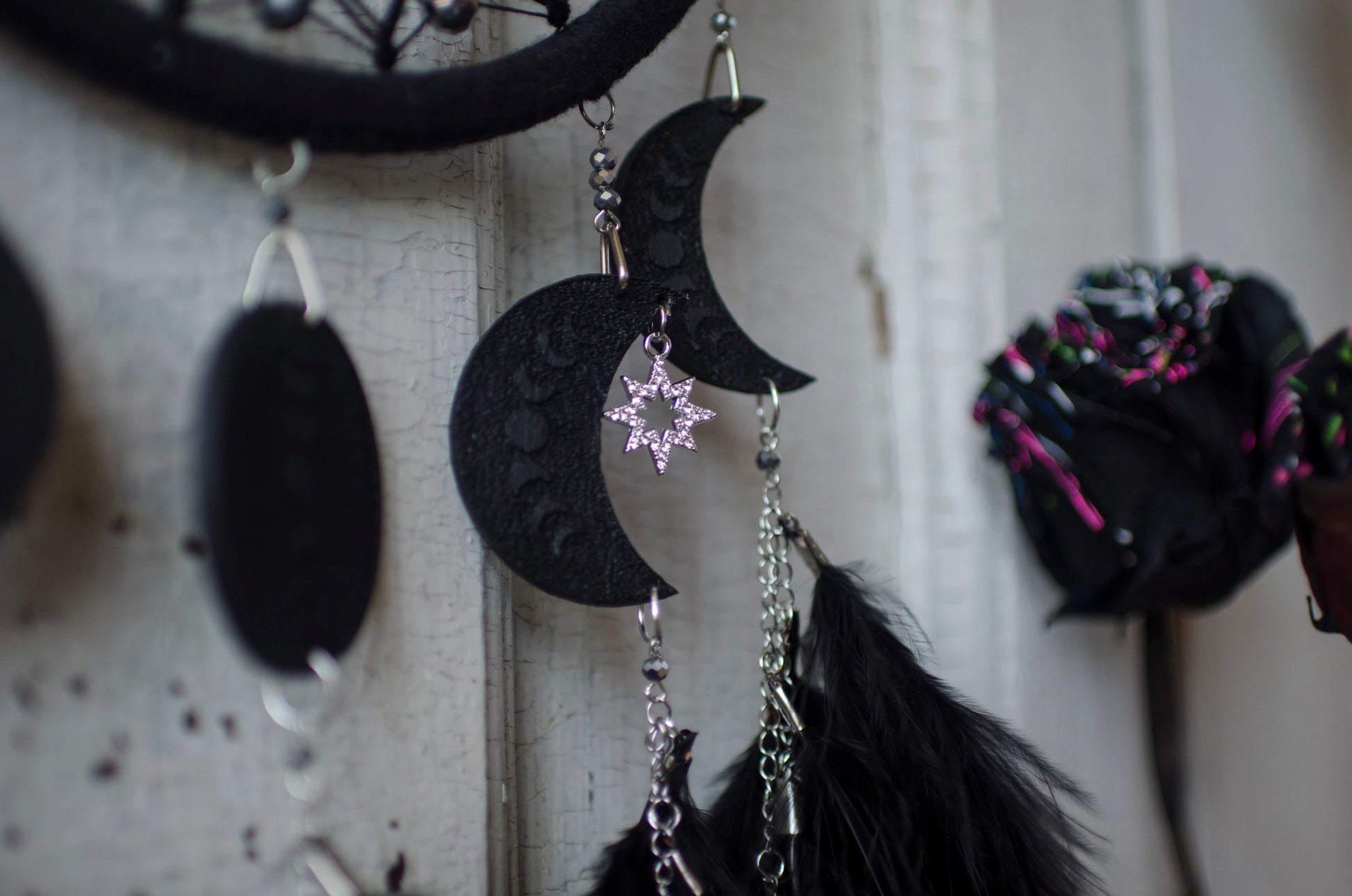 Handcrafted black dream catcher featuring a central web with black beads, adorned with five crescent moons and a central full moon, complemented by lush black feathers.