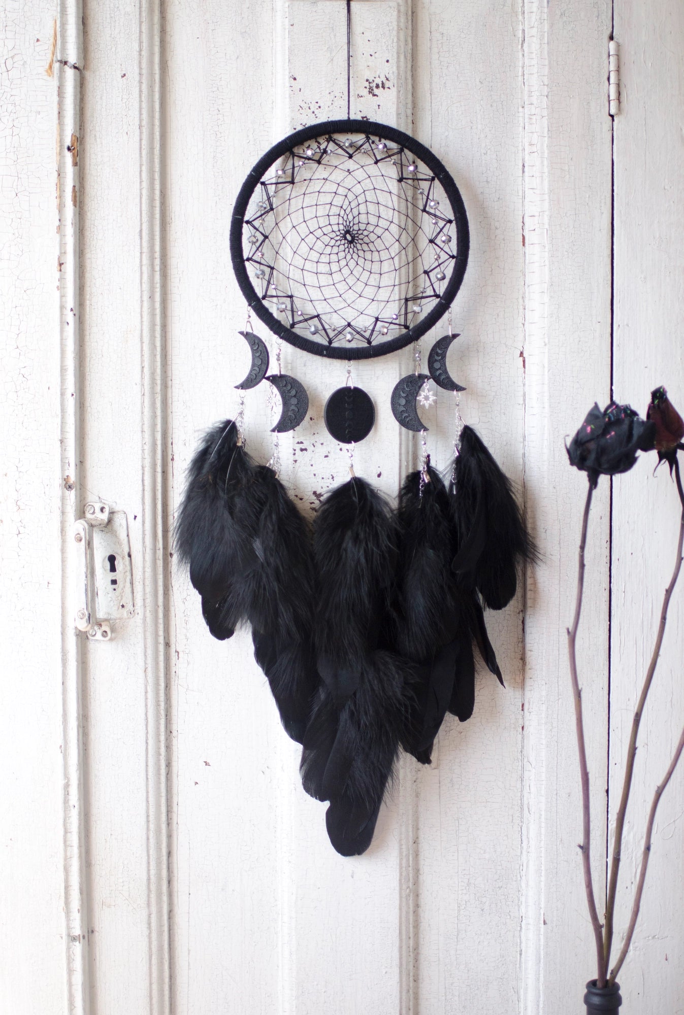 Handcrafted black dream catcher featuring a central web with black beads, adorned with five crescent moons and a central full moon, complemented by lush black feathers.