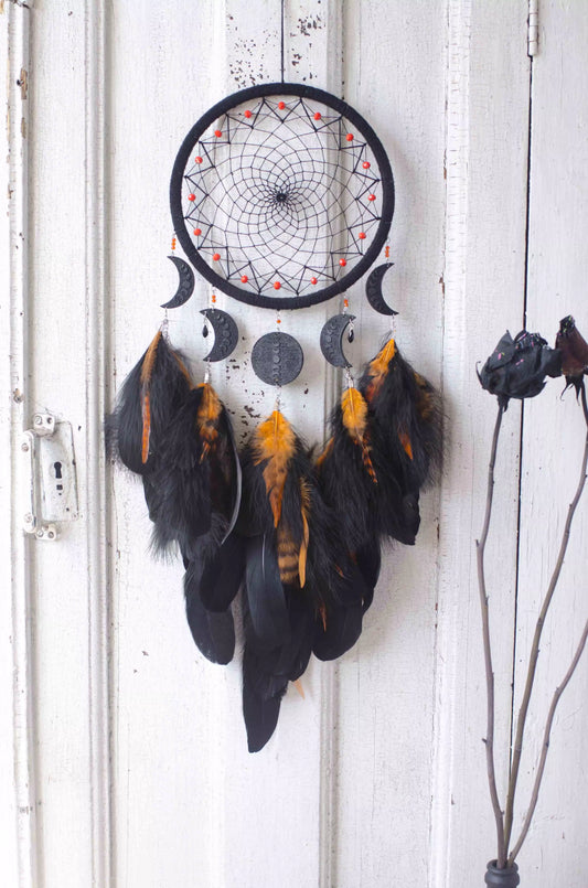 Handcrafted black dream catcher featuring an intricate web design with crescent moon charms and vibrant orange feathers. This bohemian wall decor piece is perfect for capturing negative dreams and channeling positive energy. Ideal for enhancing the aesthetic of any home or office space and makes a thoughtful, spiritual gift.