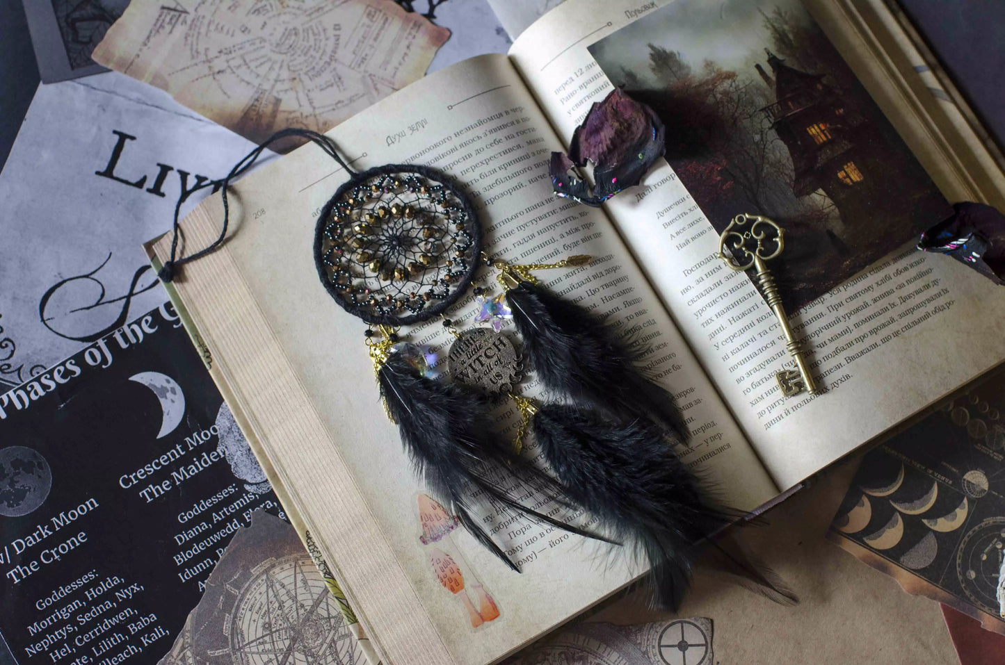 Handcrafted black witch dream catcher featuring a woven black yarn web, golden beads, black feathers, crystal moon and star charms, and a metallic 'There's a little witch in all of us' charm, designed for mystical decor and spiritual protection.