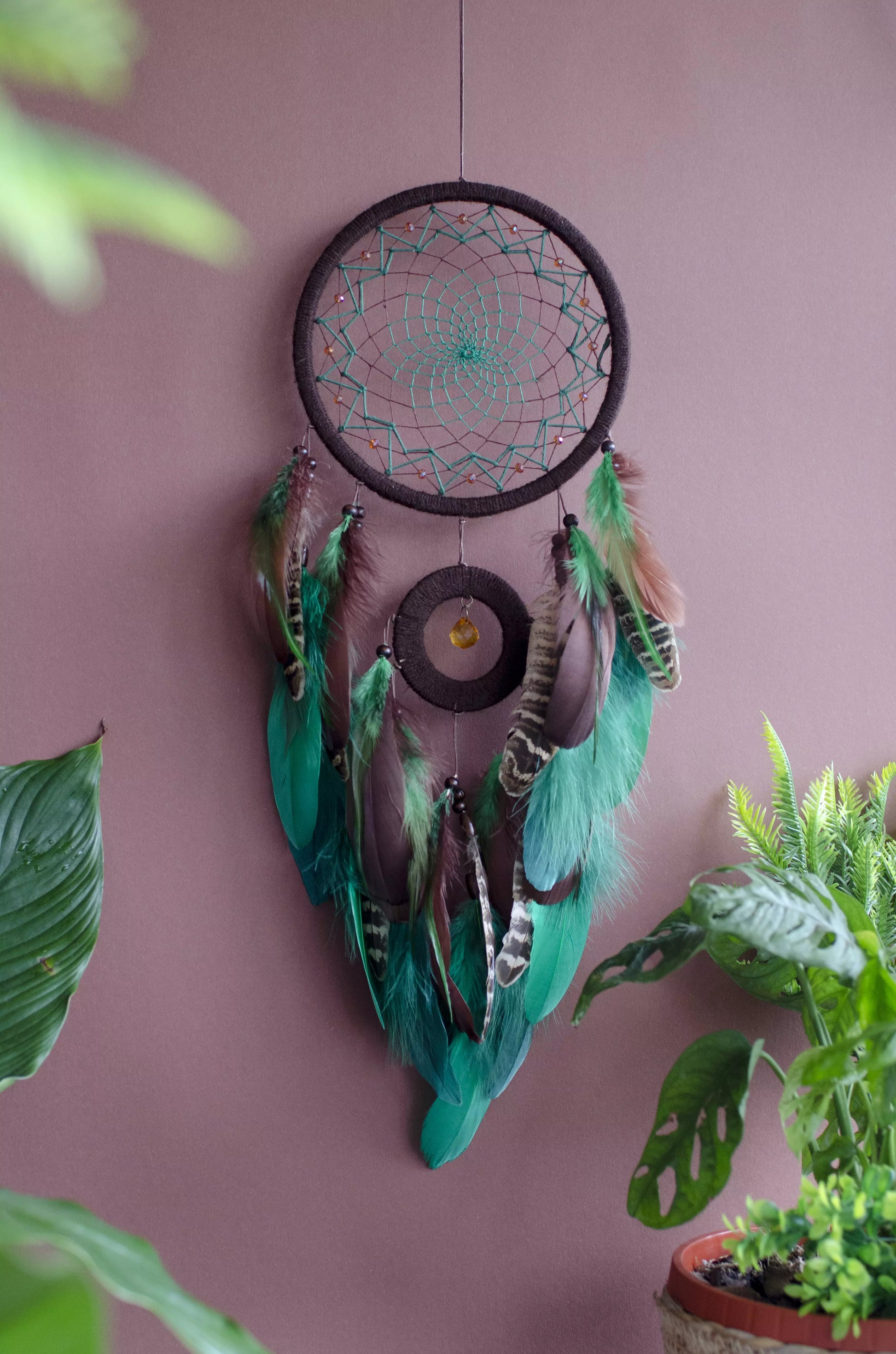 Handcrafted green dream catcher with a faceted amber crystal and natural feathers, featuring an intricate web design and earthy tones. Perfect for home decor or as a spiritual protection gift.