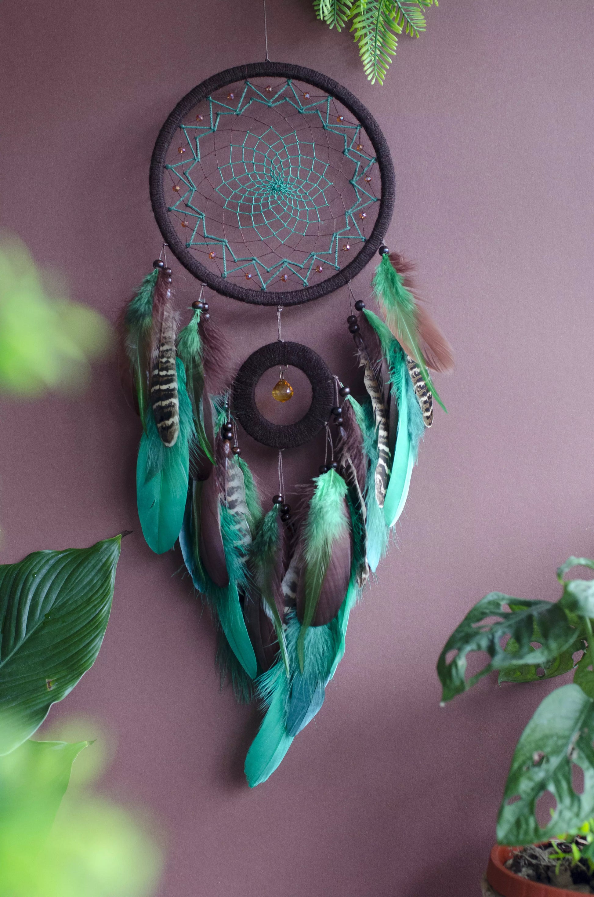 Handcrafted green dream catcher with a faceted amber crystal and natural feathers, featuring an intricate web design and earthy tones. Perfect for home decor or as a spiritual protection gift.