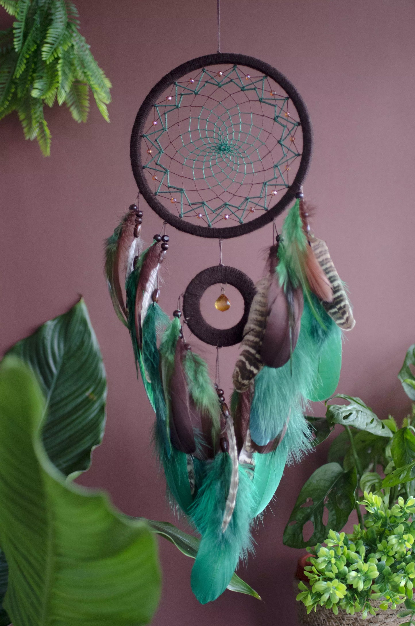 Handcrafted green dream catcher with a faceted amber crystal and natural feathers, featuring an intricate web design and earthy tones. Perfect for home decor or as a spiritual protection gift.