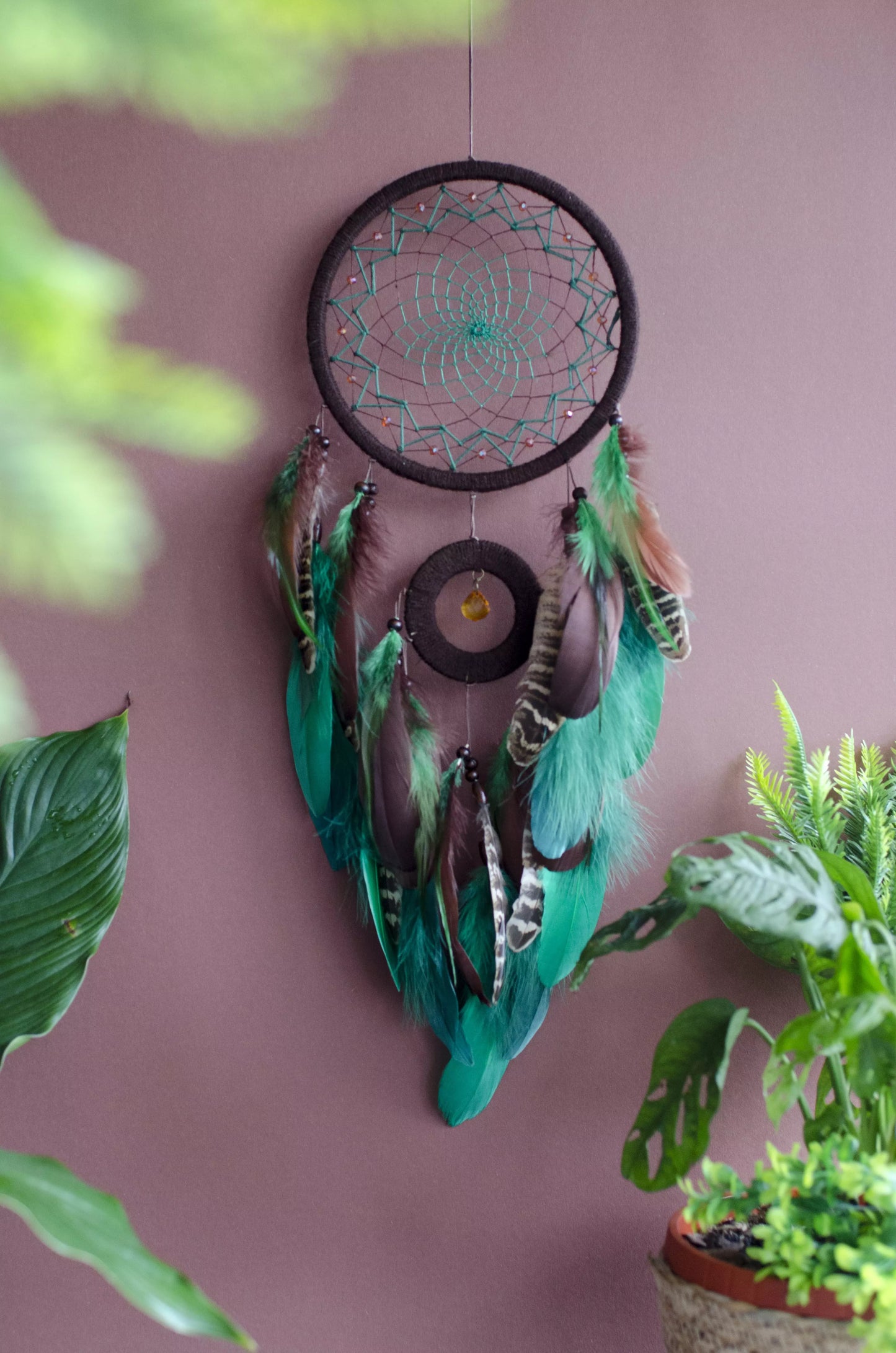 Handcrafted green dream catcher with a faceted amber crystal and natural feathers, featuring an intricate web design and earthy tones. Perfect for home decor or as a spiritual protection gift.