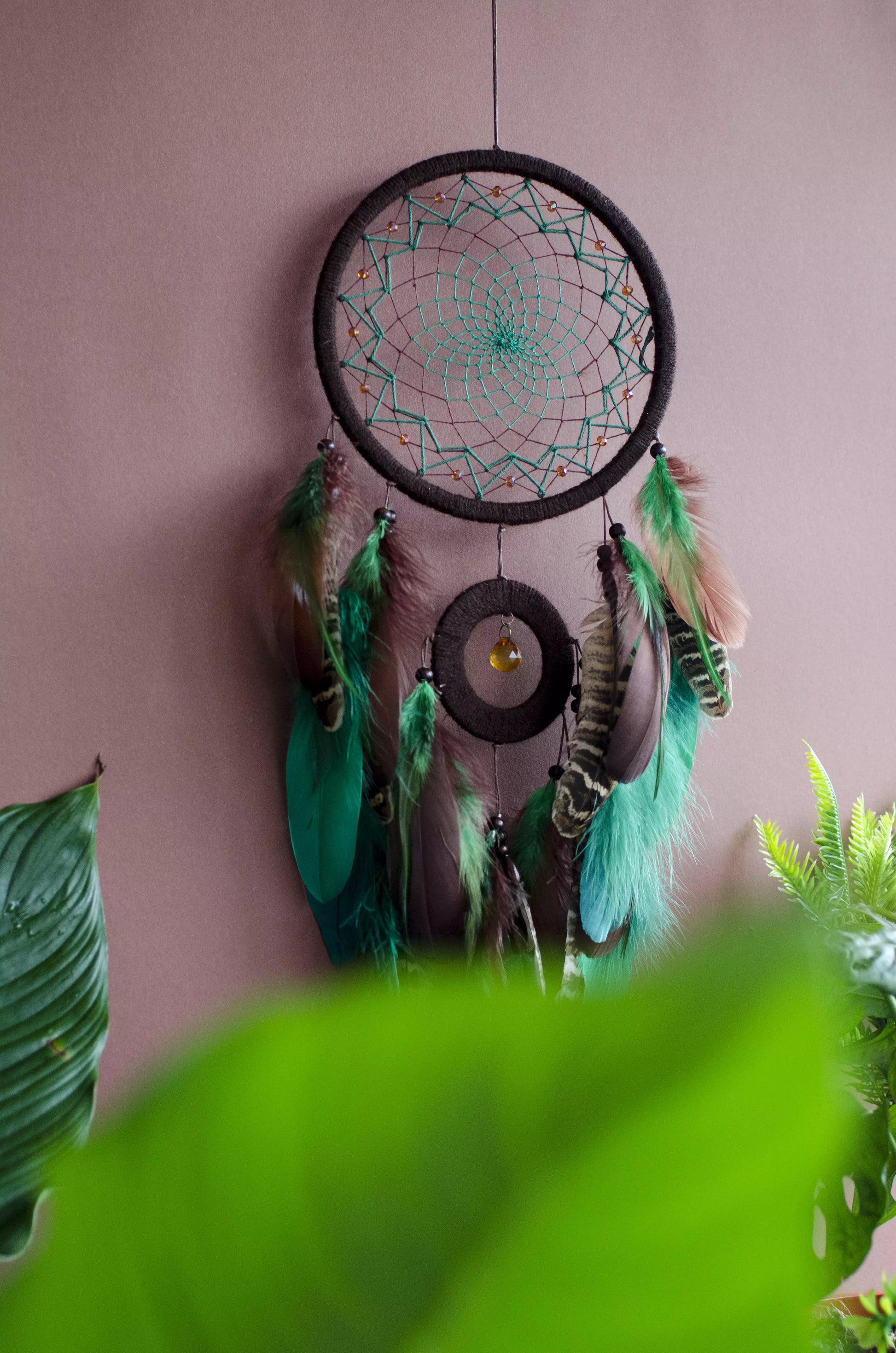 Handcrafted green dream catcher with a faceted amber crystal and natural feathers, featuring an intricate web design and earthy tones. Perfect for home decor or as a spiritual protection gift.