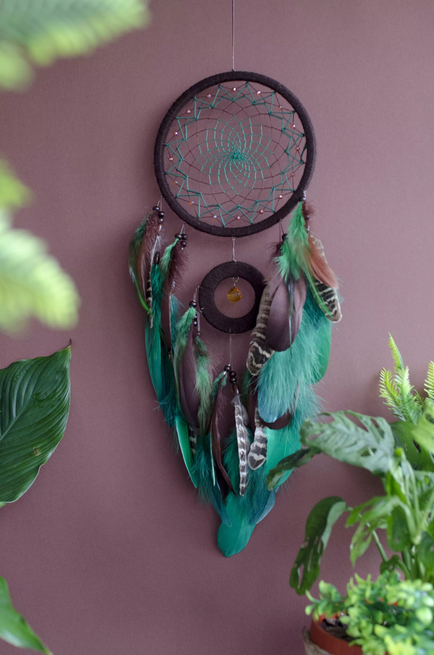 Handcrafted green dream catcher with a faceted amber crystal and natural feathers, featuring an intricate web design and earthy tones. Perfect for home decor or as a spiritual protection gift.